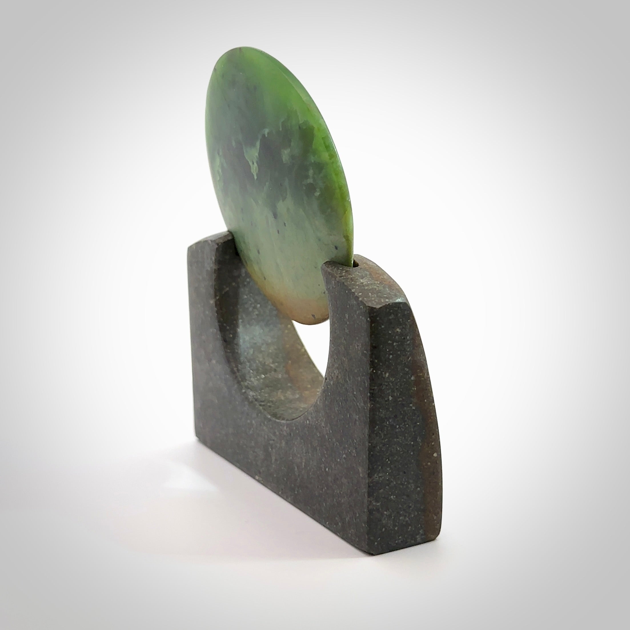 Hand carved New Zealand Flower Jade Disc with Greywacke stand sculpture. Hand carved here in New Zealand by Ric Moor. This is a 'one only' sculpture, a beautiful display piece. Small Jade disc sculpture for desk.