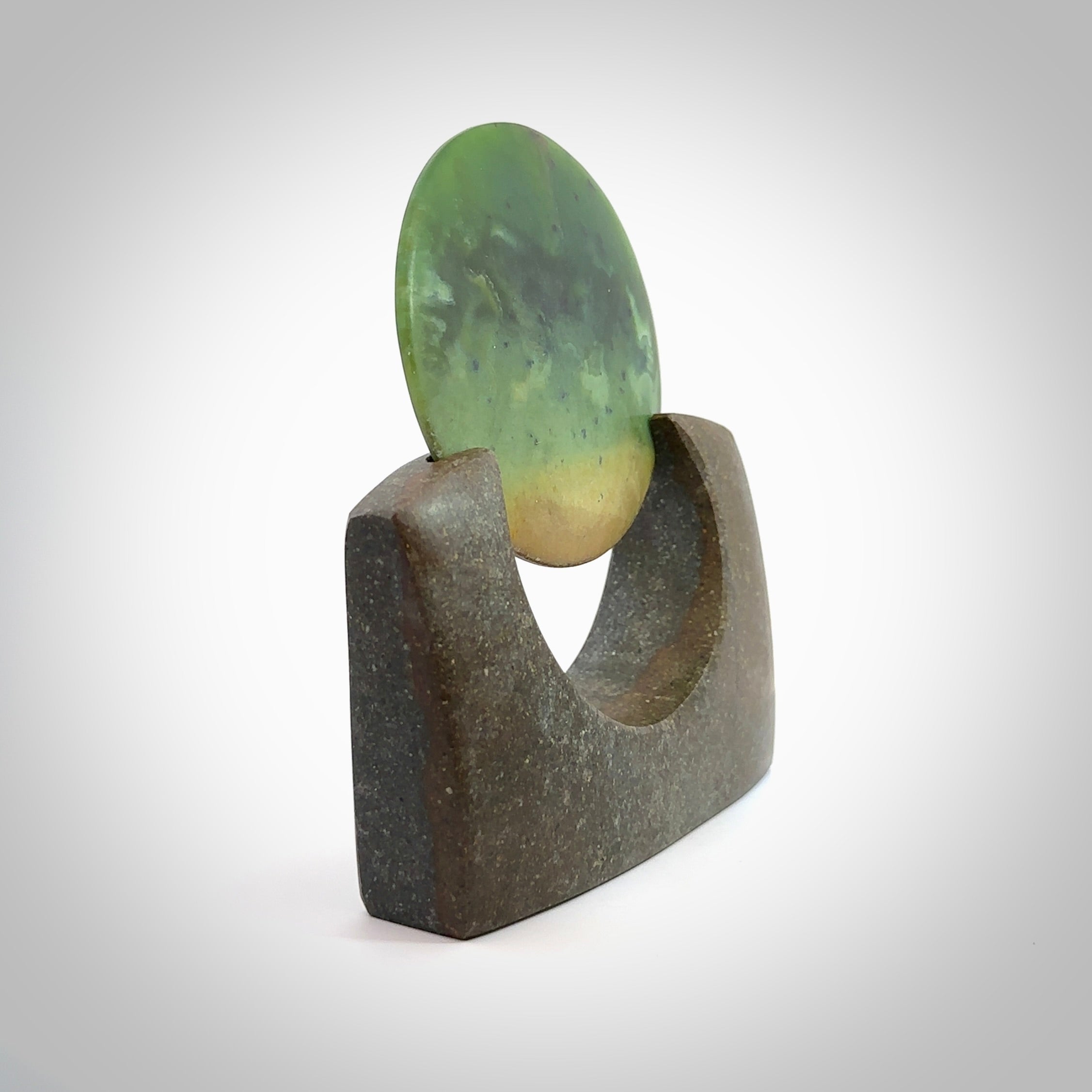 Hand carved New Zealand Flower Jade Disc with Greywacke stand sculpture. Hand carved here in New Zealand by Ric Moor. This is a 'one only' sculpture, a beautiful display piece. Small Jade disc sculpture for desk.