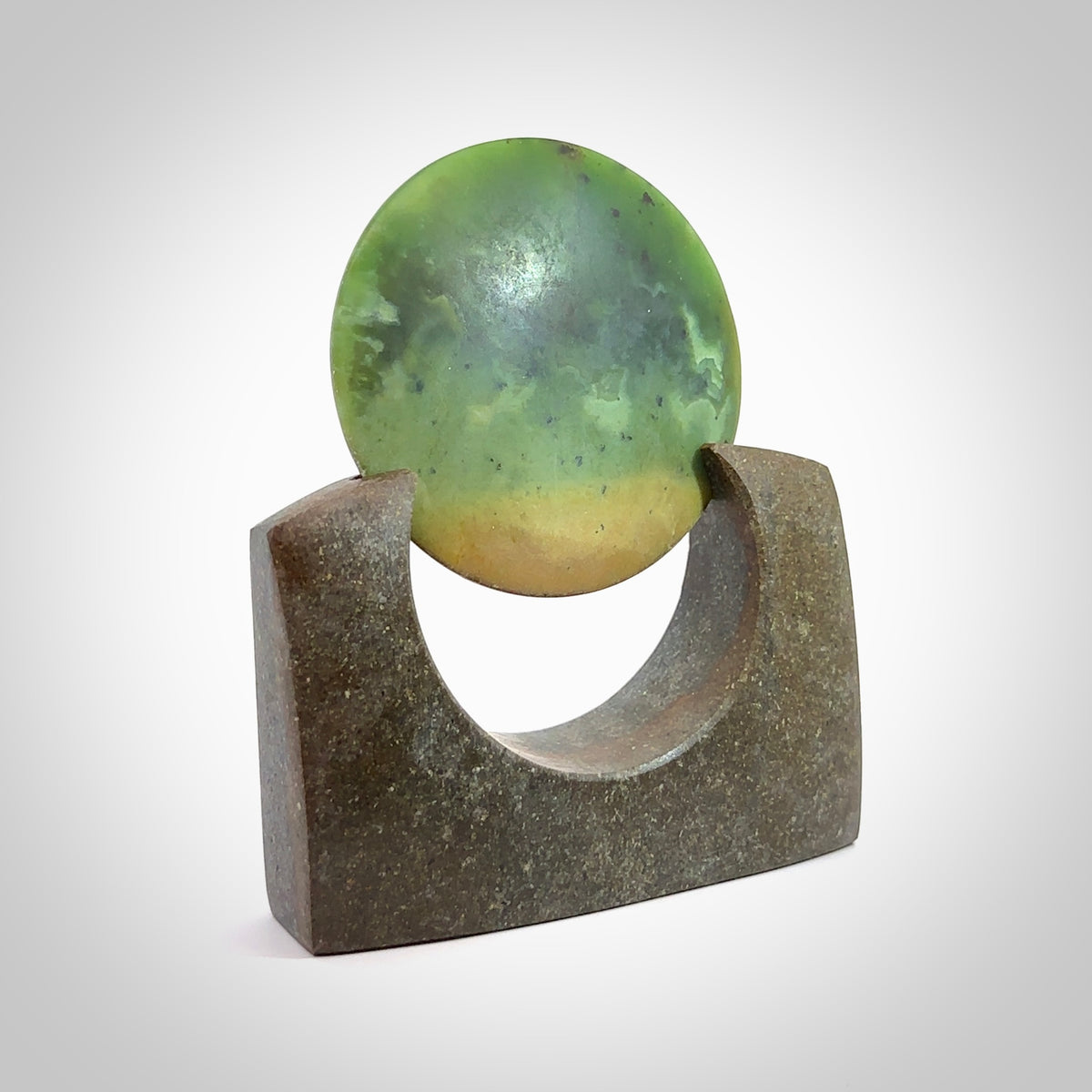 Hand carved New Zealand Flower Jade Disc with Greywacke stand sculpture. Hand carved here in New Zealand by Ric Moor. This is a 'one only' sculpture, a beautiful display piece. Small Jade disc sculpture for desk.