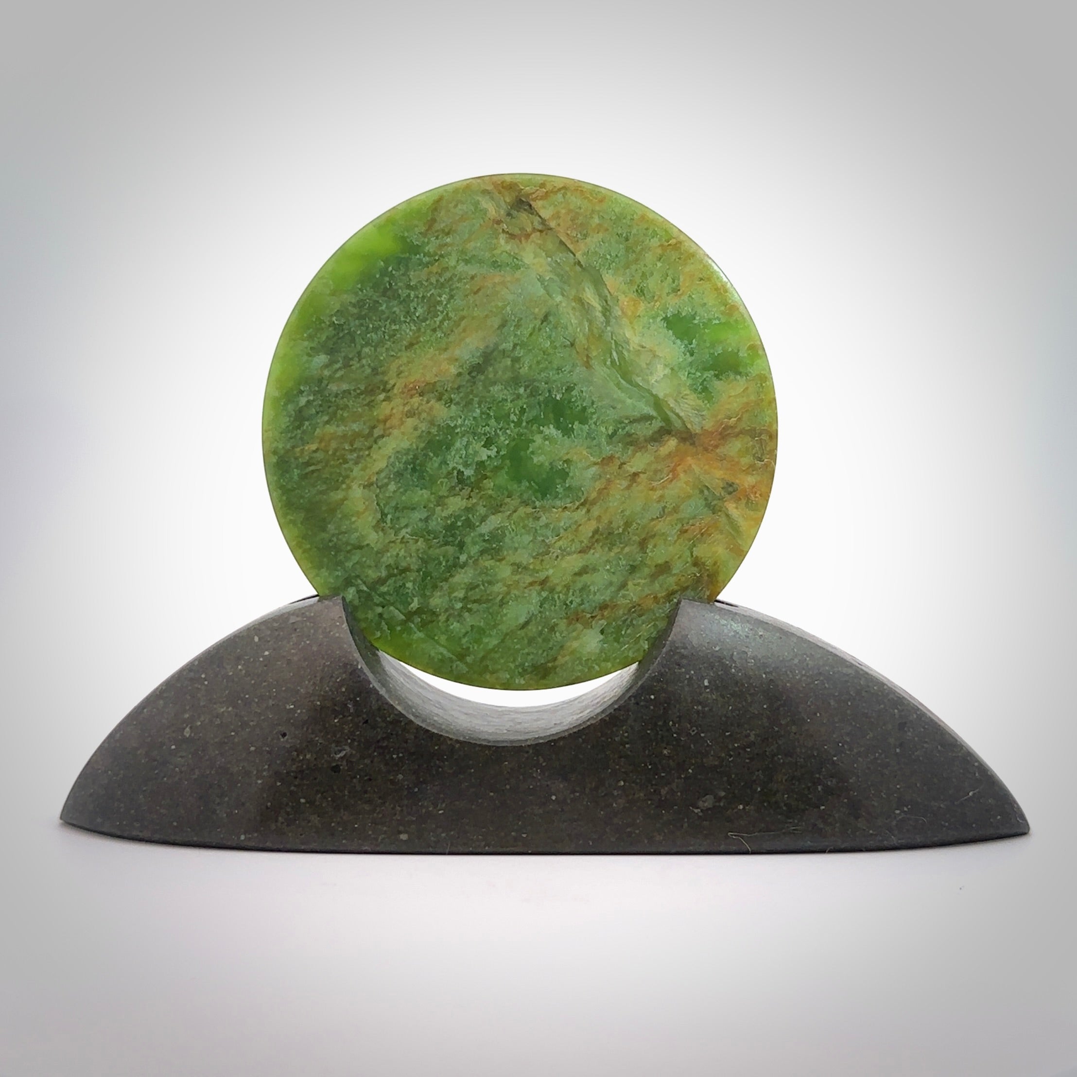 Hand carved New Zealand Flower Jade Disc with Greywacke stand sculpture. Hand carved here in New Zealand by Ric Moor. This is a 'one only' sculpture, a beautiful display piece. Small Jade disc sculpture for desk.