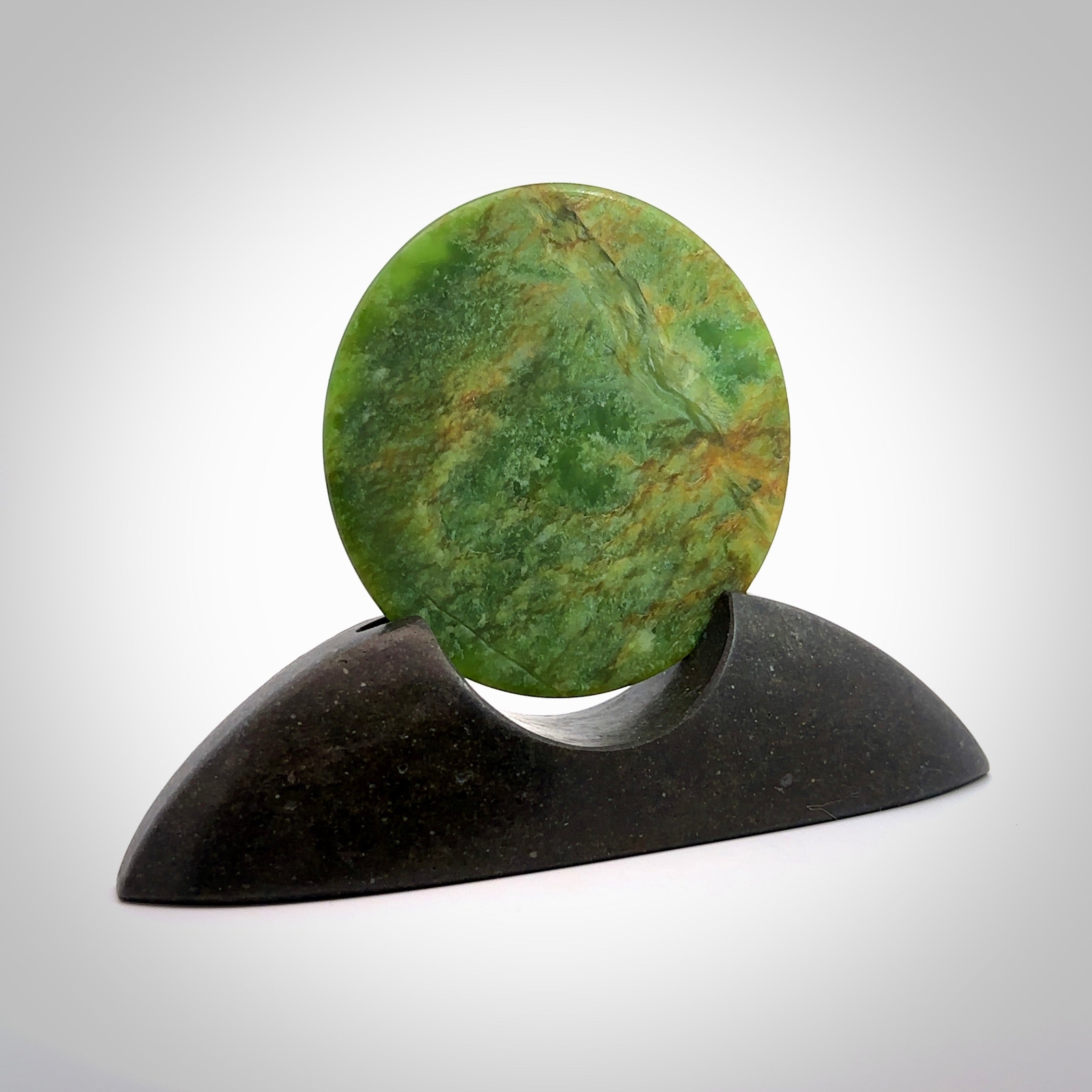 Hand carved New Zealand Flower Jade Disc with Greywacke stand sculpture. Hand carved here in New Zealand by Ric Moor. This is a 'one only' sculpture, a beautiful display piece. Small Jade disc sculpture for desk.