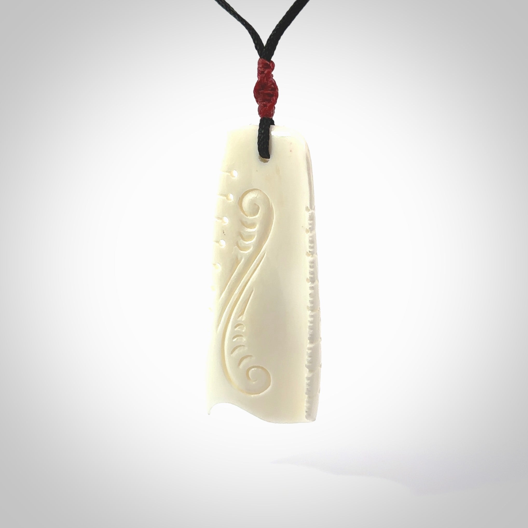 A hand carved contemporary bone toki pendant. The cord and binding is black and the cord is adjustable. Medium hand made etched toki with Koru engraving necklace. One off work of art to wear. Delivered in a woven kete pouch.