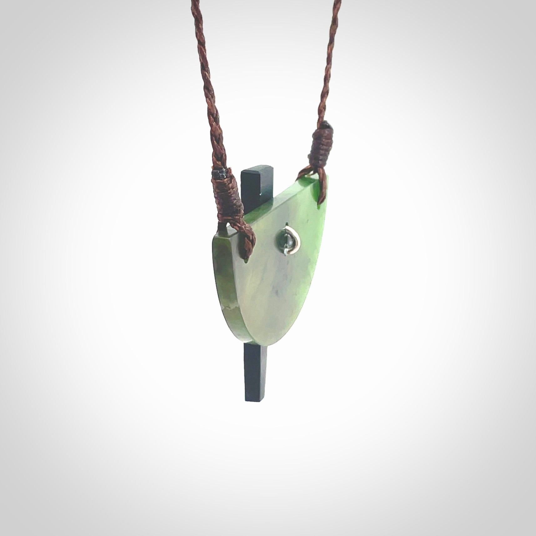 This piece is a contemporary shield pendant carved from jade from New Zealand. It is a deep green colour. The cord is brown and is length adjustable. Hand made with Australian Black Jade and Jade.