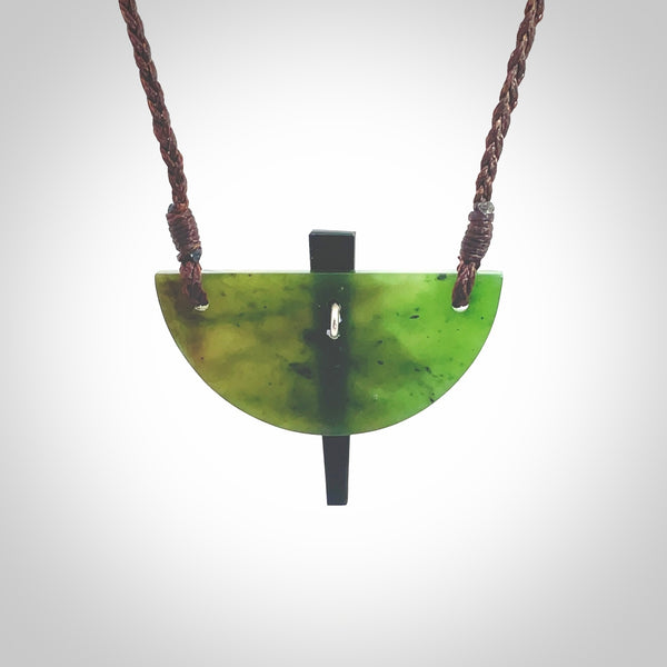 This piece is a contemporary shield pendant carved from jade from New Zealand. It is a deep green colour. The cord is brown and is length adjustable. Hand made with Australian Black Jade and Jade.
