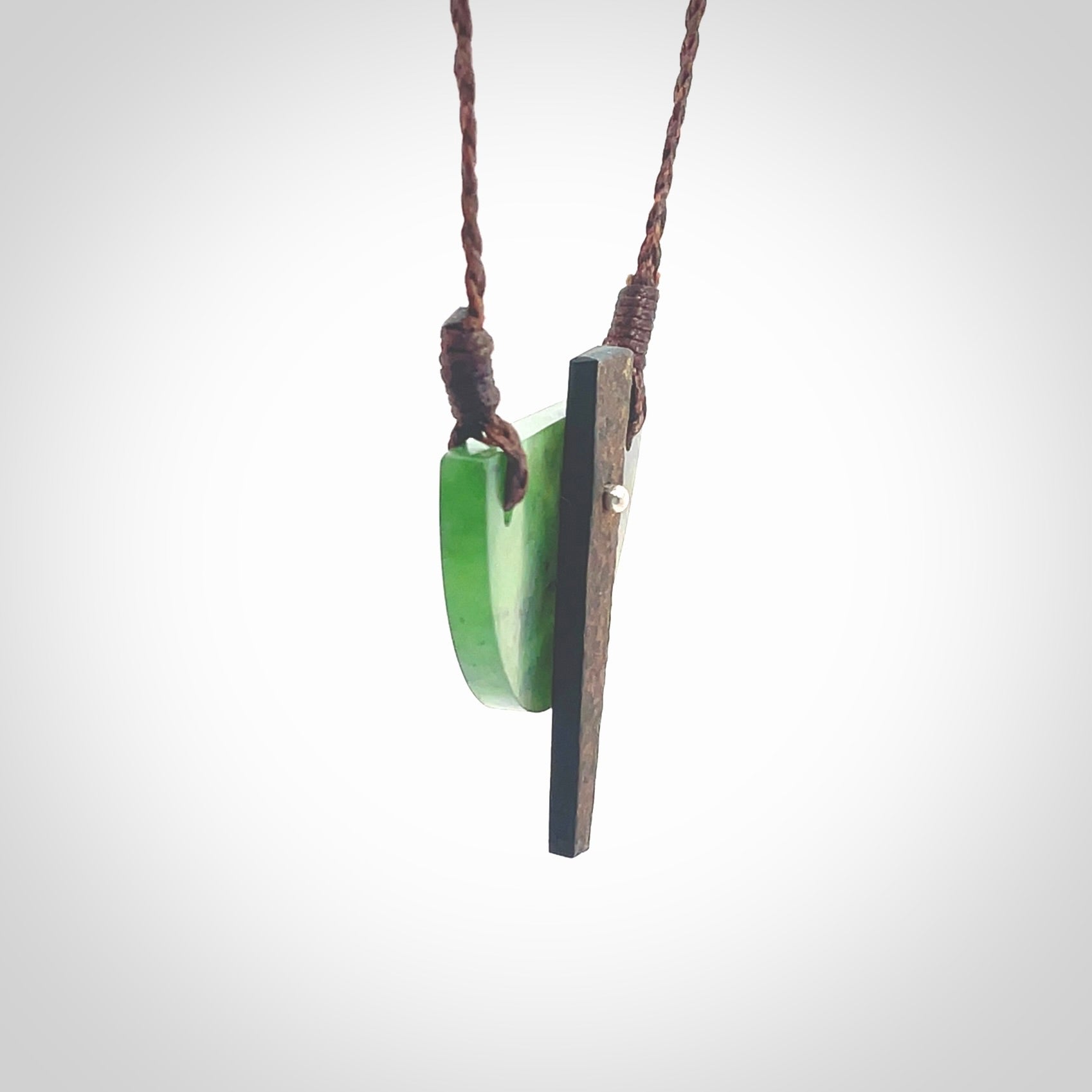 This piece is a contemporary shield pendant carved from jade from New Zealand. It is a deep green colour. The cord is brown and is length adjustable. Hand made with Australian Black Jade and Jade.