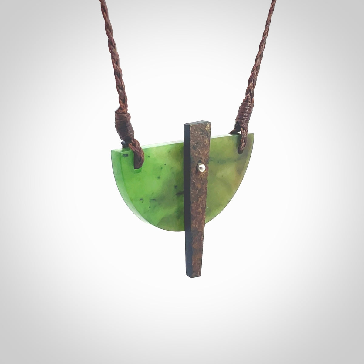 This piece is a contemporary shield pendant carved from jade from New Zealand. It is a deep green colour. The cord is brown and is length adjustable. Hand made with Australian Black Jade and Jade.