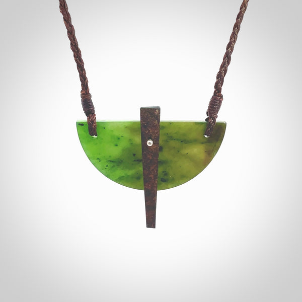 This piece is a contemporary shield pendant carved from jade from New Zealand. It is a deep green colour. The cord is brown and is length adjustable. Hand made with Australian Black Jade and Jade.