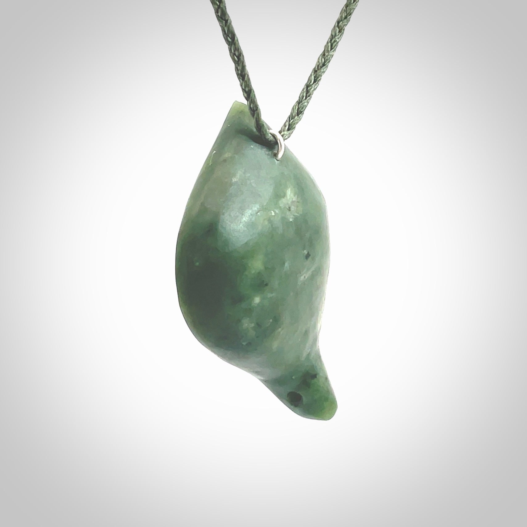 This picture shows a hand carved drop pendant made from a deep green coloured New Zealand Pounamu, jade. The front face is a concave, cupped design and the back is round. It is provided with an adjustable fern green cord in a woven kete pouch. Shipped to you with Express Courier.