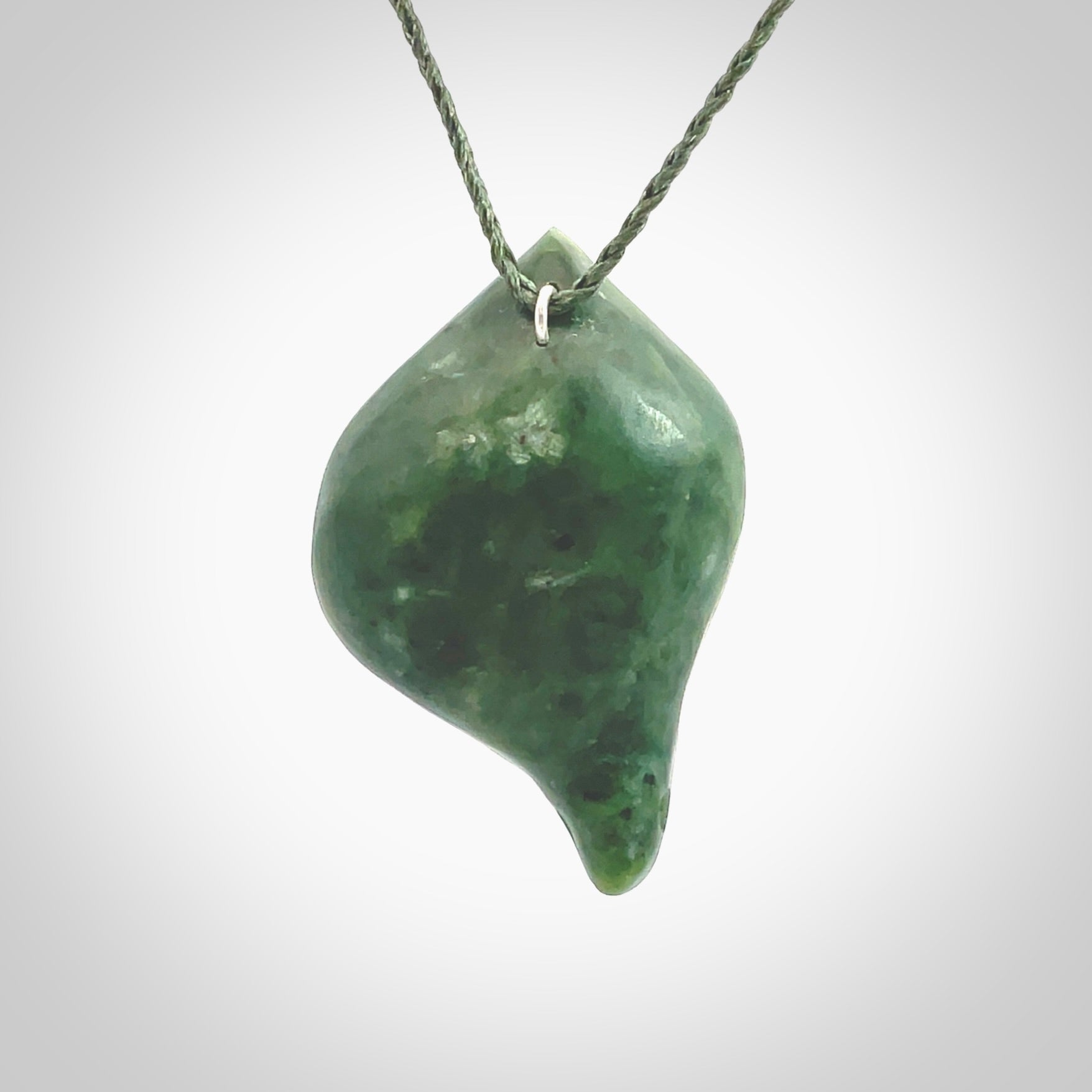 This picture shows a hand carved drop pendant made from a deep green coloured New Zealand Pounamu, jade. The front face is a concave, cupped design and the back is round. It is provided with an adjustable fern green cord in a woven kete pouch. Shipped to you with Express Courier.