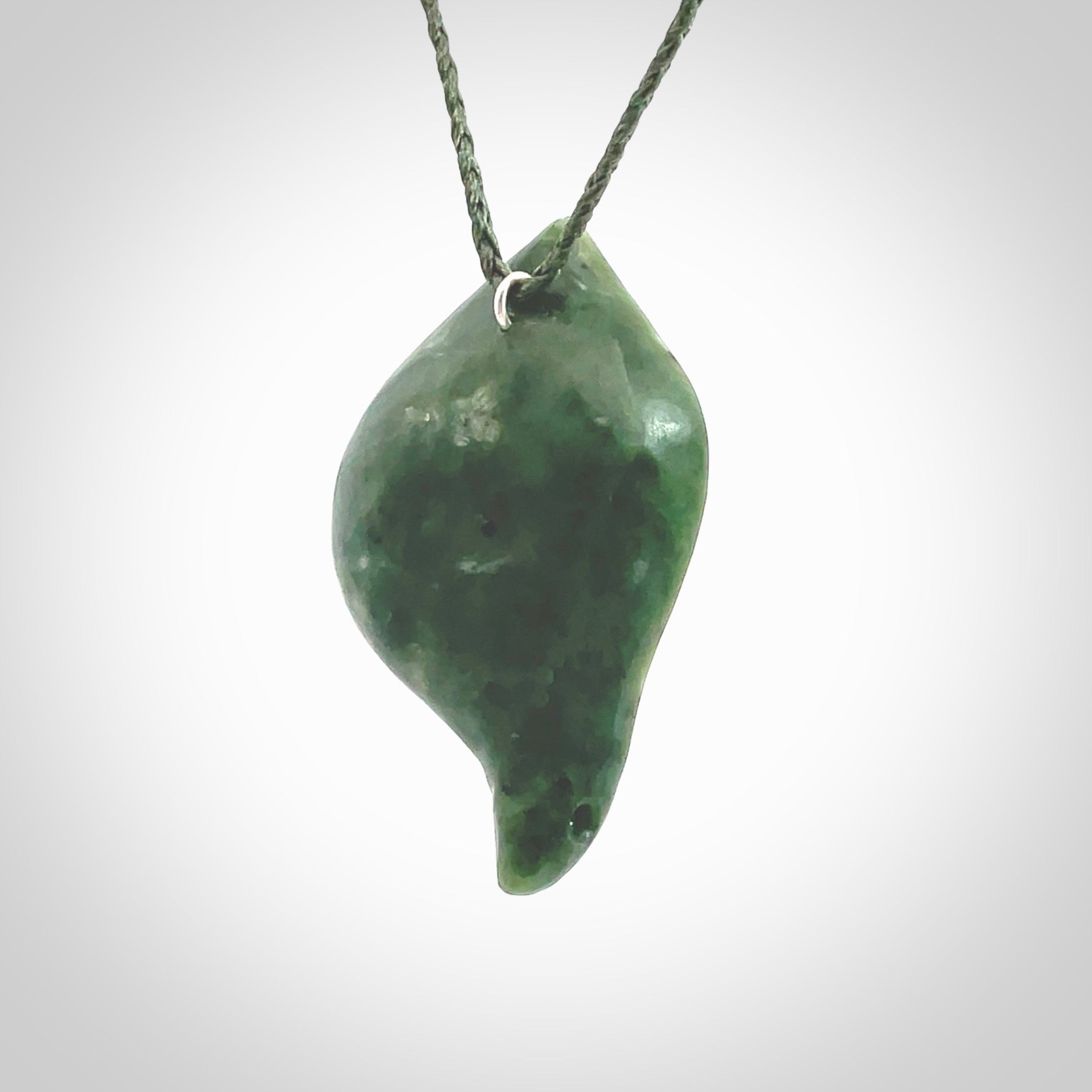 This picture shows a hand carved drop pendant made from a deep green coloured New Zealand Pounamu, jade. The front face is a concave, cupped design and the back is round. It is provided with an adjustable fern green cord in a woven kete pouch. Shipped to you with Express Courier.