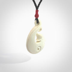 Hand carved bone hook pendant hand made by Peter Mitchell in New Zealand. This bone hook is provided with an adjustable black cord and packaged in a woven kete pouch. Free delivery worldwide.