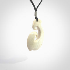 Hand carved bone hook pendant hand made by Peter Mitchell in New Zealand. This bone hook is provided with an adjustable black cord and packaged in a woven kete pouch. Free delivery worldwide.