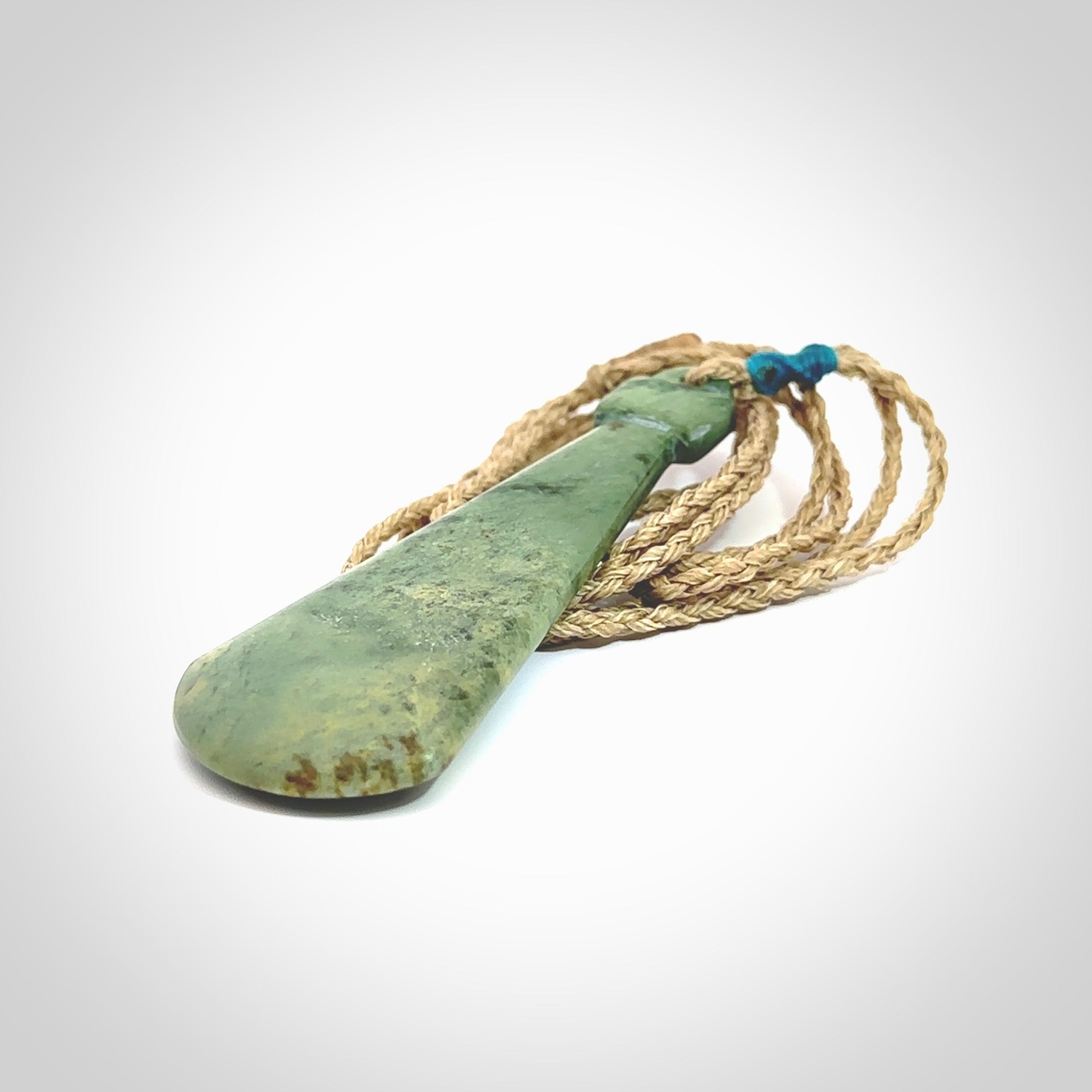 This is a sleek and slender hand carved New Zealand Jade mere pendant. The stone is a light green with mottled inclusions. The cord is tan and adjustable. The pendant has a light polish and just glows. Delivered in a woven kete pouch.