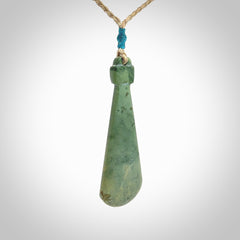 This is a sleek and slender hand carved New Zealand Jade mere pendant. The stone is a light green with mottled inclusions. The cord is tan and adjustable. The pendant has a light polish and just glows. Delivered in a woven kete pouch.