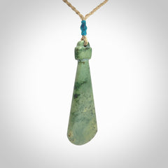 This is a sleek and slender hand carved New Zealand Jade mere pendant. The stone is a light green with mottled inclusions. The cord is tan and adjustable. The pendant has a light polish and just glows. Delivered in a woven kete pouch.