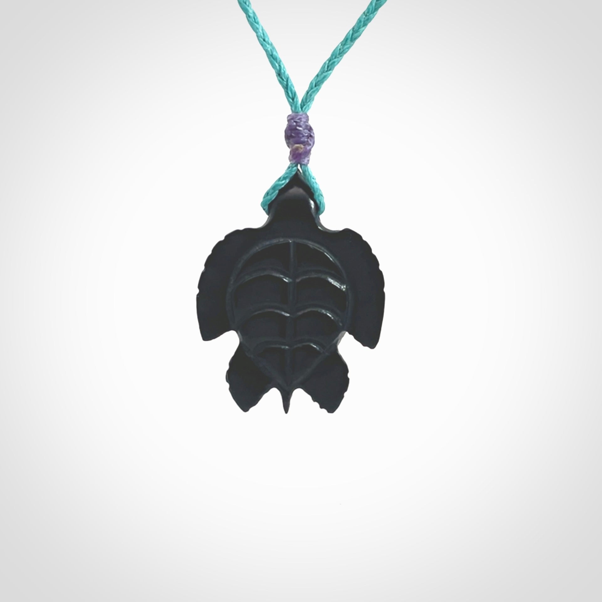 This picture shows a hand carved black jade turtle pendant. It is polished to a soft shine and has quite a lot of detail carved into the jade. The cord is a hand plaited Paradise Blue, waxed polyester. Carved by NZ Pacific.