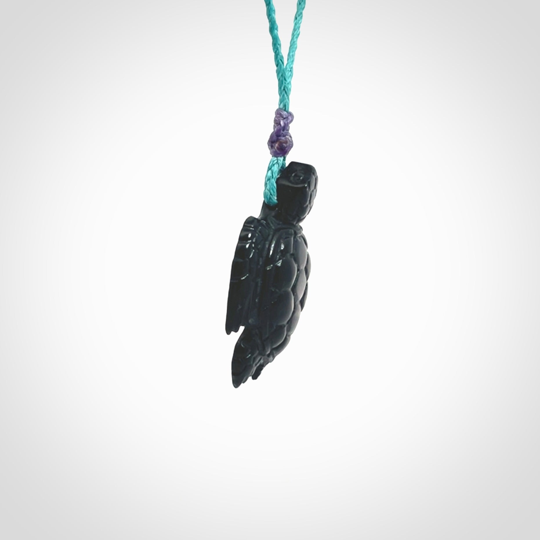 This picture shows a hand carved black jade turtle pendant. It is polished to a soft shine and has quite a lot of detail carved into the jade. The cord is a hand plaited Paradise Blue, waxed polyester. Carved by NZ Pacific.