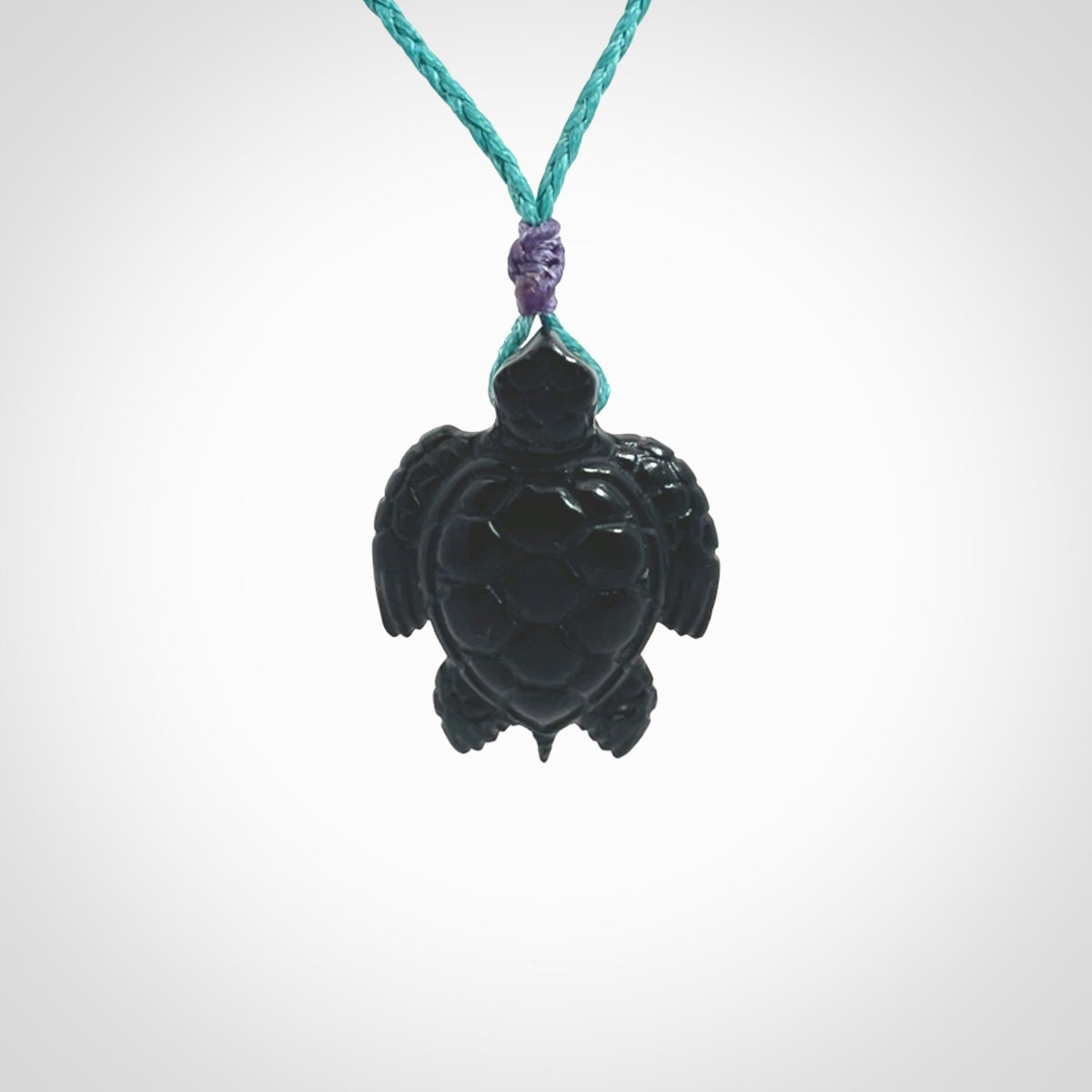 This picture shows a hand carved black jade turtle pendant. It is polished to a soft shine and has quite a lot of detail carved into the jade. The cord is a hand plaited Paradise Blue, waxed polyester. Carved by NZ Pacific.