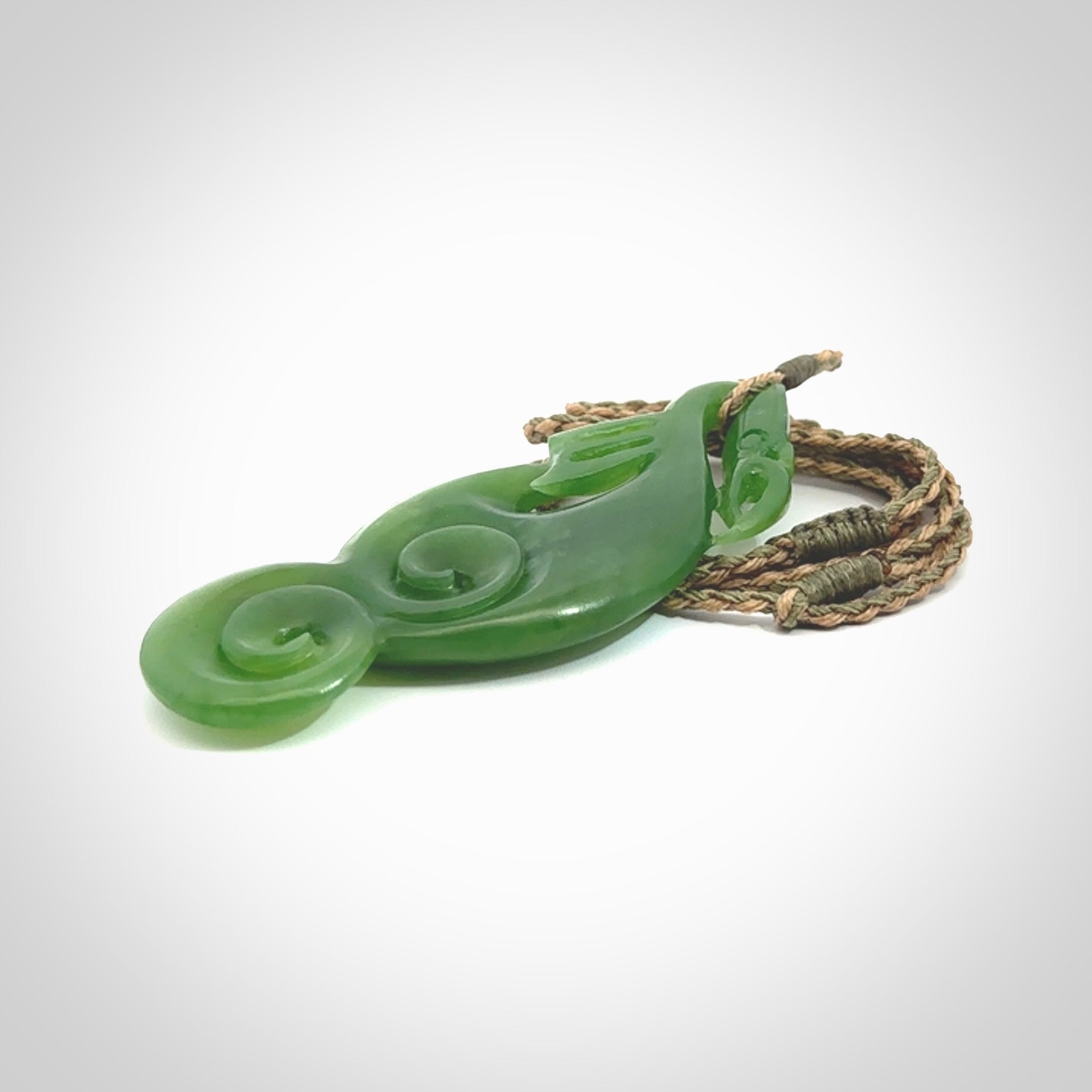 This pendant is a beautiful large New Zealand Auhunga green jade manaia pendant with koru. It has the head of a bird and the tail of a fish and also two koru carved into the body. It is carved by Ross Crump here in New Zealand. Provided with an adjustable tan/khaki cord.