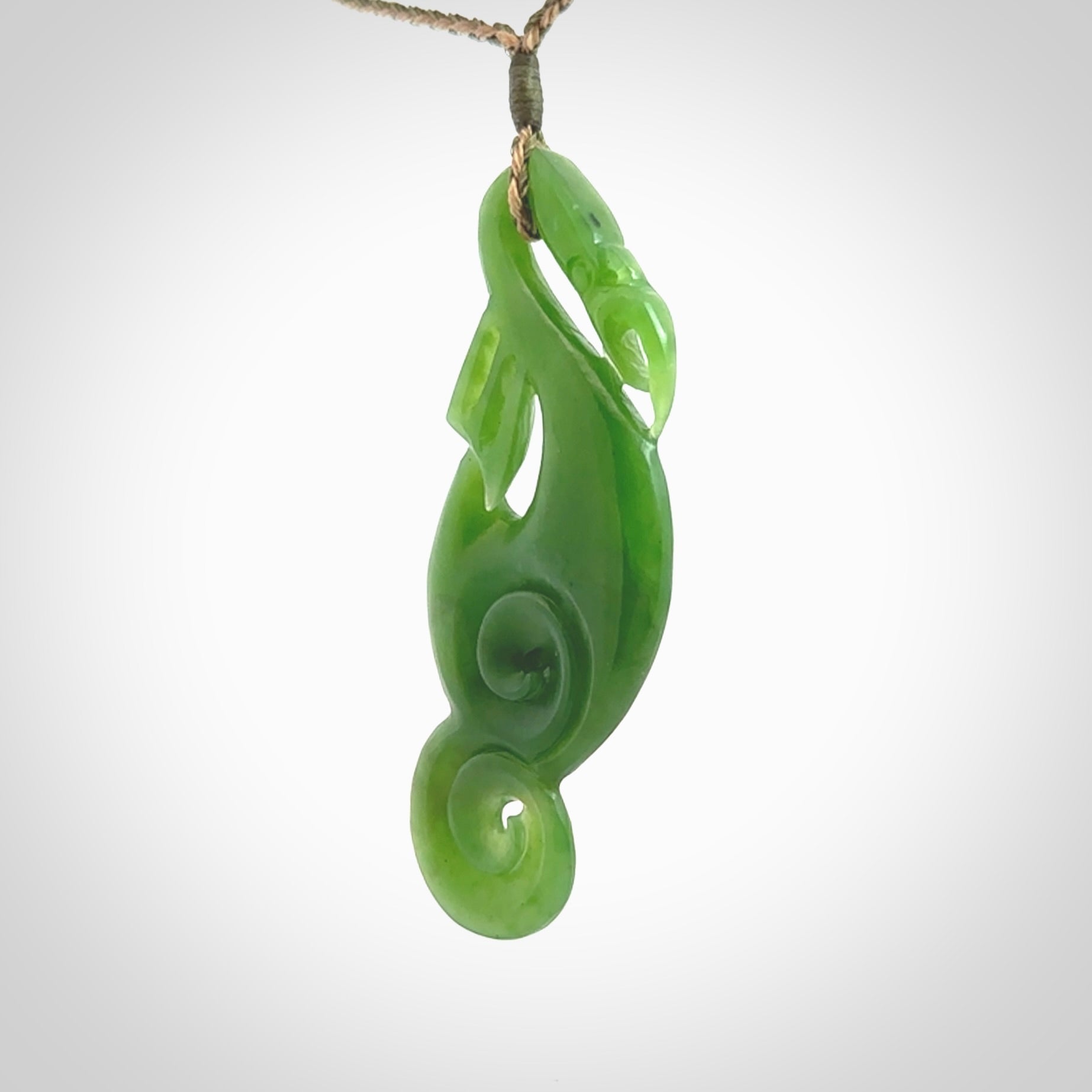 This pendant is a beautiful large New Zealand Auhunga green jade manaia pendant with koru. It has the head of a bird and the tail of a fish and also two koru carved into the body. It is carved by Ross Crump here in New Zealand. Provided with an adjustable tan/khaki cord.