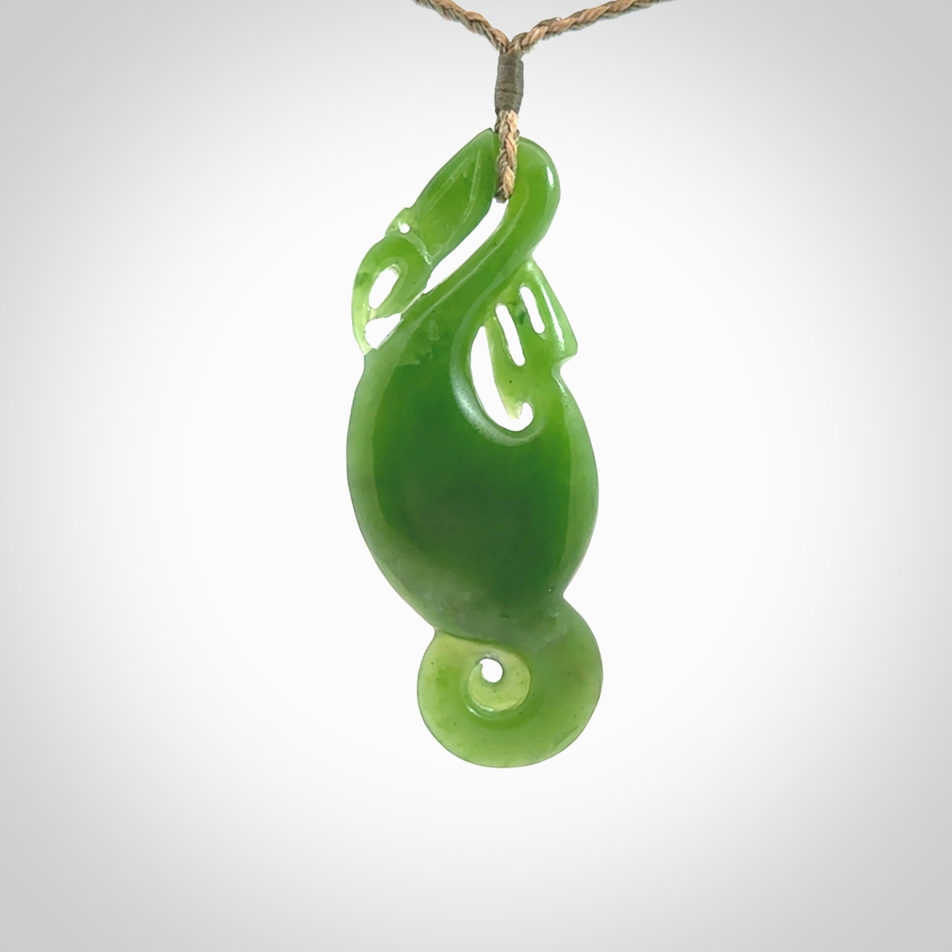 This pendant is a beautiful large New Zealand Auhunga green jade manaia pendant with koru. It has the head of a bird and the tail of a fish and also two koru carved into the body. It is carved by Ross Crump here in New Zealand. Provided with an adjustable tan/khaki cord.