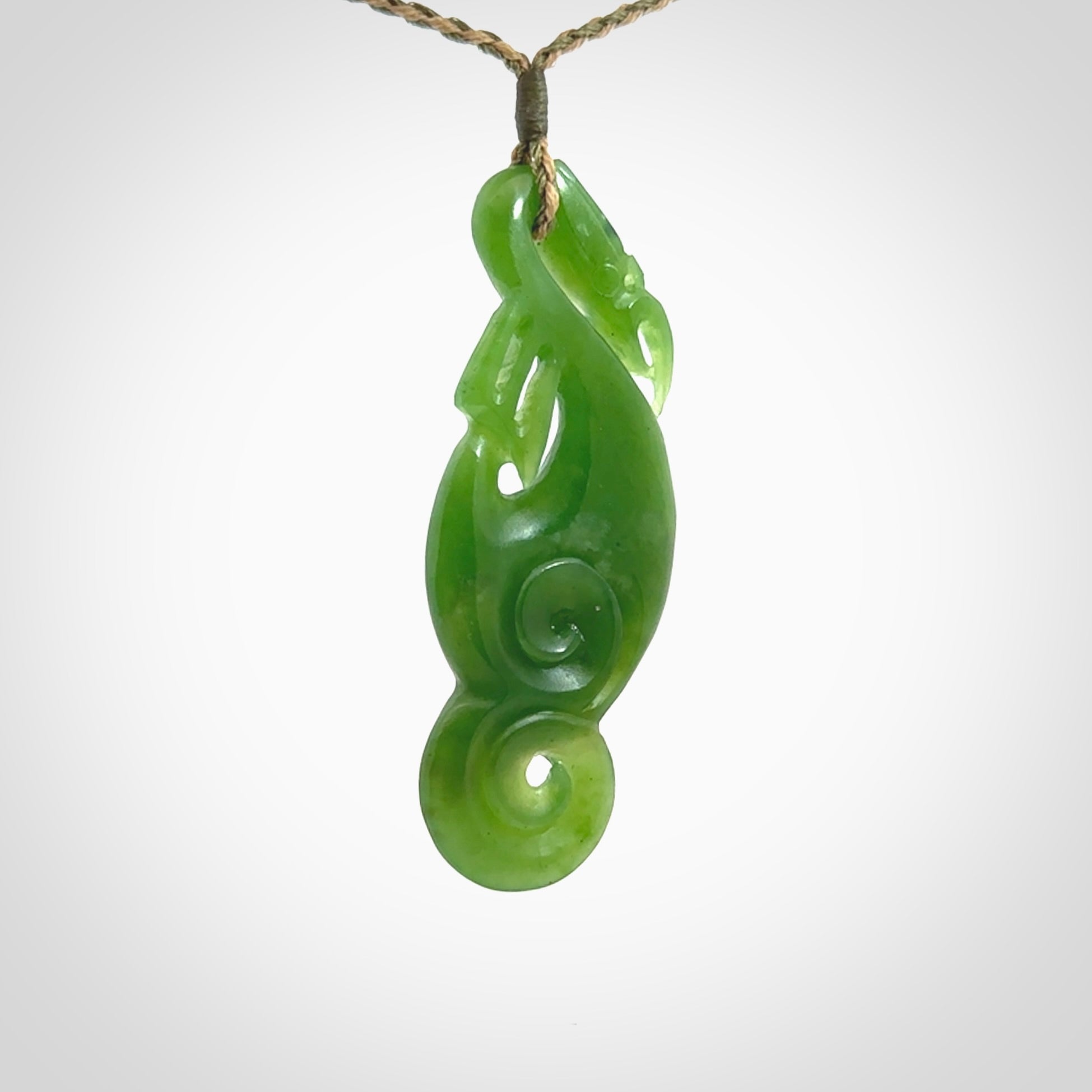 This pendant is a beautiful large New Zealand Auhunga green jade manaia pendant with koru. It has the head of a bird and the tail of a fish and also two koru carved into the body. It is carved by Ross Crump here in New Zealand. Provided with an adjustable tan/khaki cord.