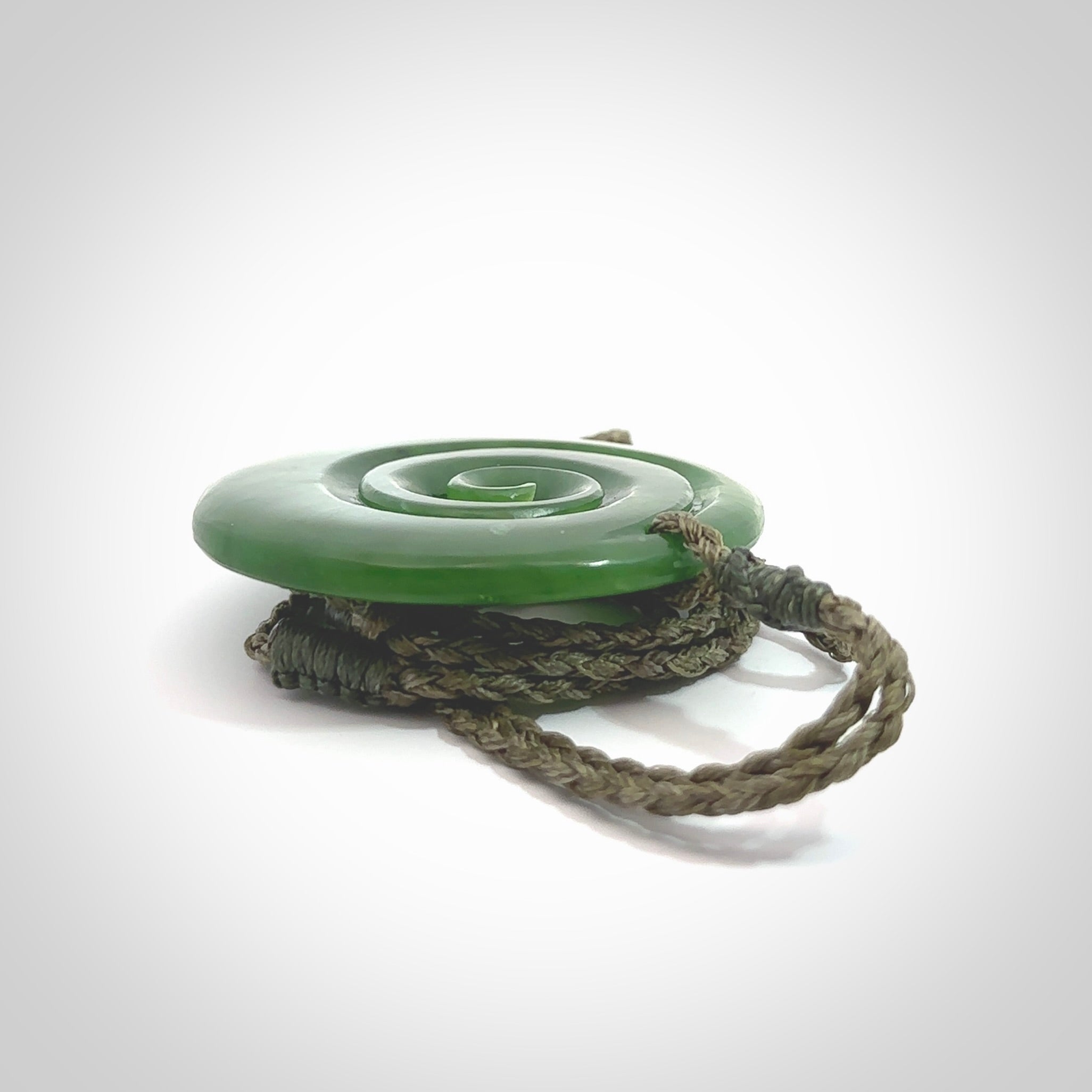 This picture shows a detailed koru carving. A pendant carved from a lovely piece of New Zealand jade, Pounamu. We have suspended this necklace on a hand plaited cord in Khaki and you can adjust its length so that you can position the pendant where it suits you best.