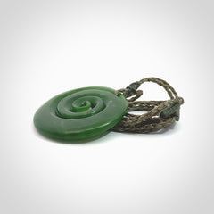 This picture shows a detailed koru carving. A pendant carved from a lovely piece of New Zealand jade, Pounamu. We have suspended this necklace on a hand plaited cord in Khaki and you can adjust its length so that you can position the pendant where it suits you best.