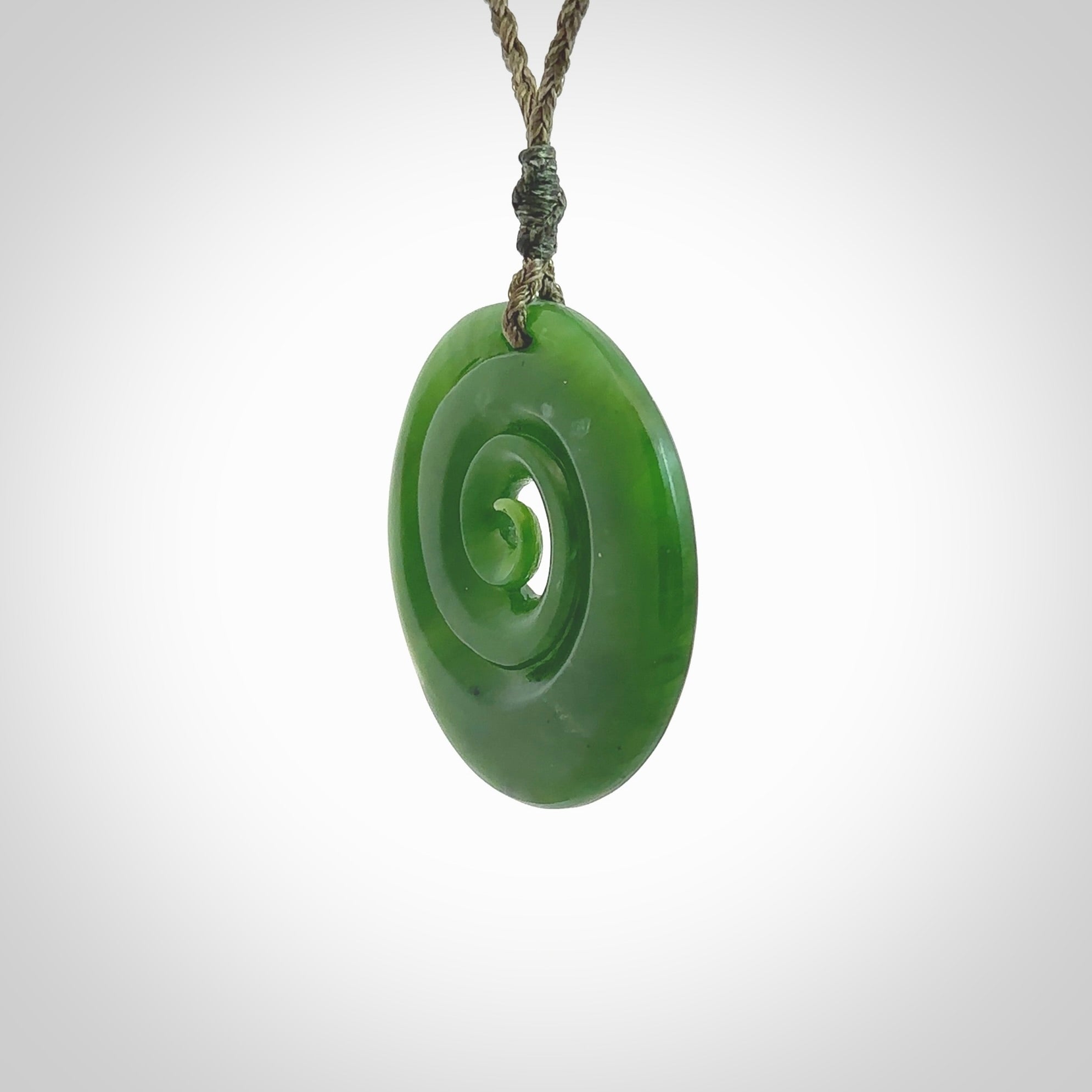 This picture shows a detailed koru carving. A pendant carved from a lovely piece of New Zealand jade, Pounamu. We have suspended this necklace on a hand plaited cord in Khaki and you can adjust its length so that you can position the pendant where it suits you best.