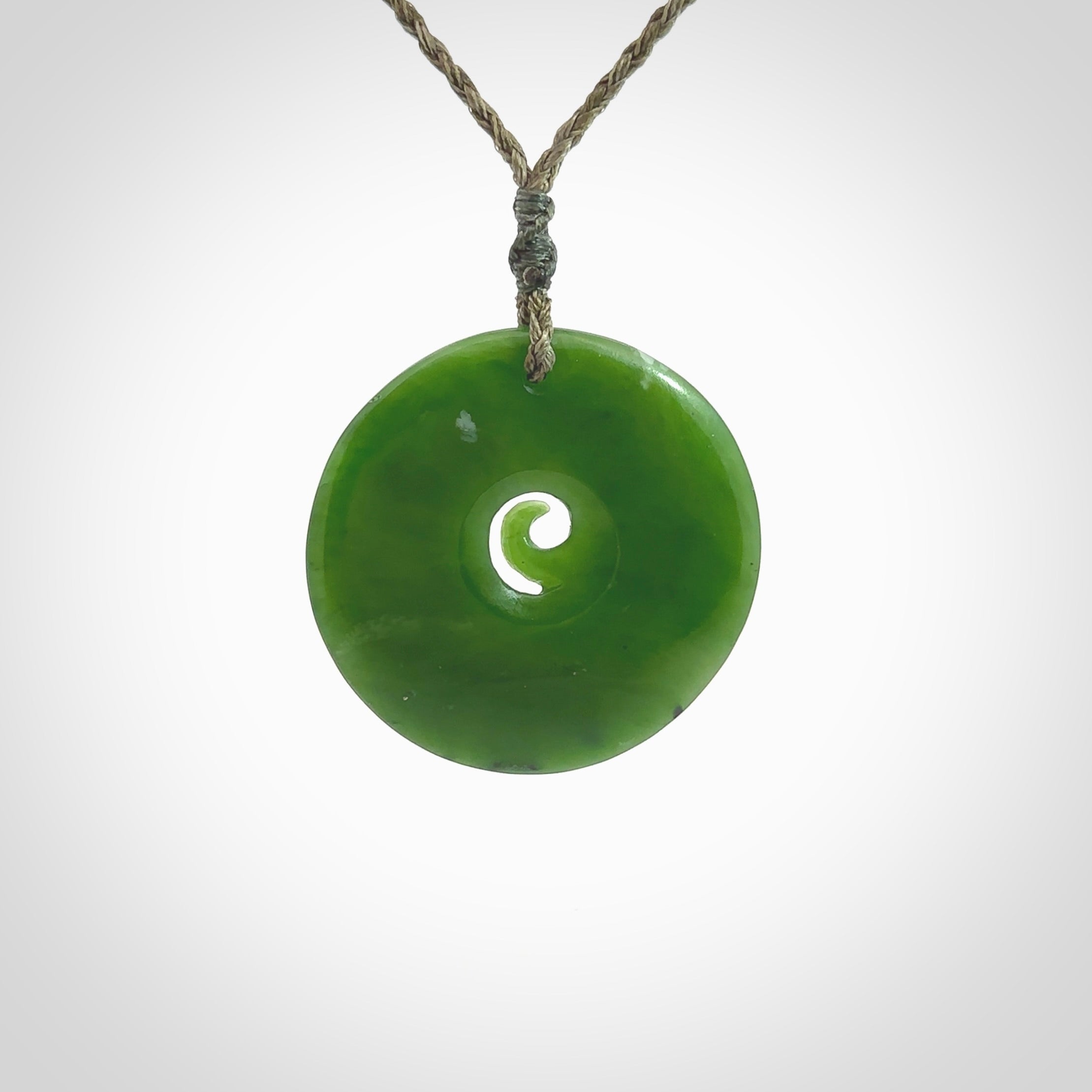 This picture shows a detailed koru carving. A pendant carved from a lovely piece of New Zealand jade, Pounamu. We have suspended this necklace on a hand plaited cord in Khaki and you can adjust its length so that you can position the pendant where it suits you best.