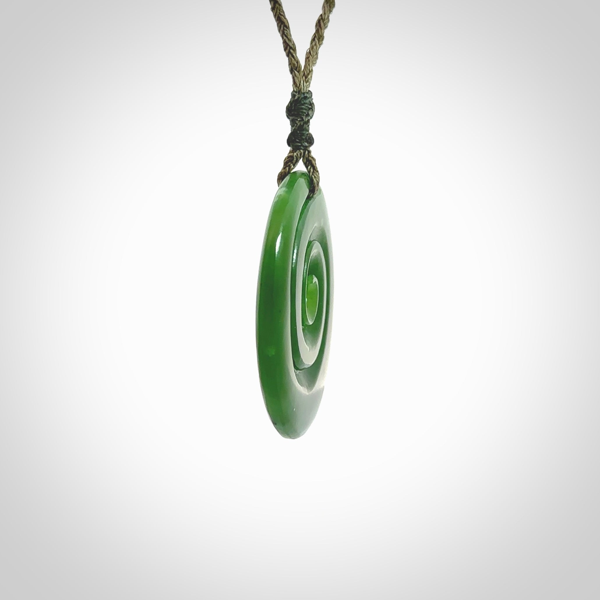 This picture shows a detailed koru carving. A pendant carved from a lovely piece of New Zealand jade, Pounamu. We have suspended this necklace on a hand plaited cord in Khaki and you can adjust its length so that you can position the pendant where it suits you best.