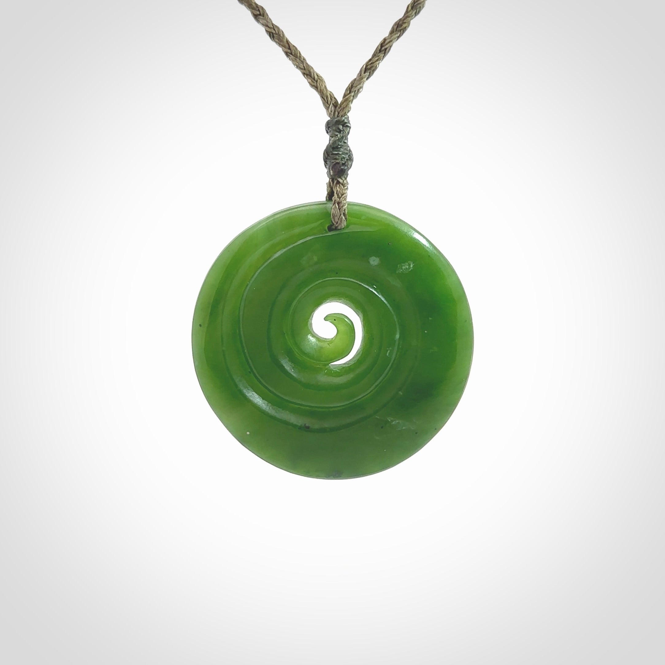 This picture shows a detailed koru carving. A pendant carved from a lovely piece of New Zealand jade, Pounamu. We have suspended this necklace on a hand plaited cord in Khaki and you can adjust its length so that you can position the pendant where it suits you best.