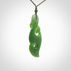 This picture shows a polished manaia pendant carved for us by Ross Crump. It is a dark matte green colour in traditional manaia design. Ross has added a koru on the bottom which elongates the carving and gives it some decorative flair. We have added a 4-Plait cord in olive green and made it length adjustable. This is a very beautiful piece of art to wear.