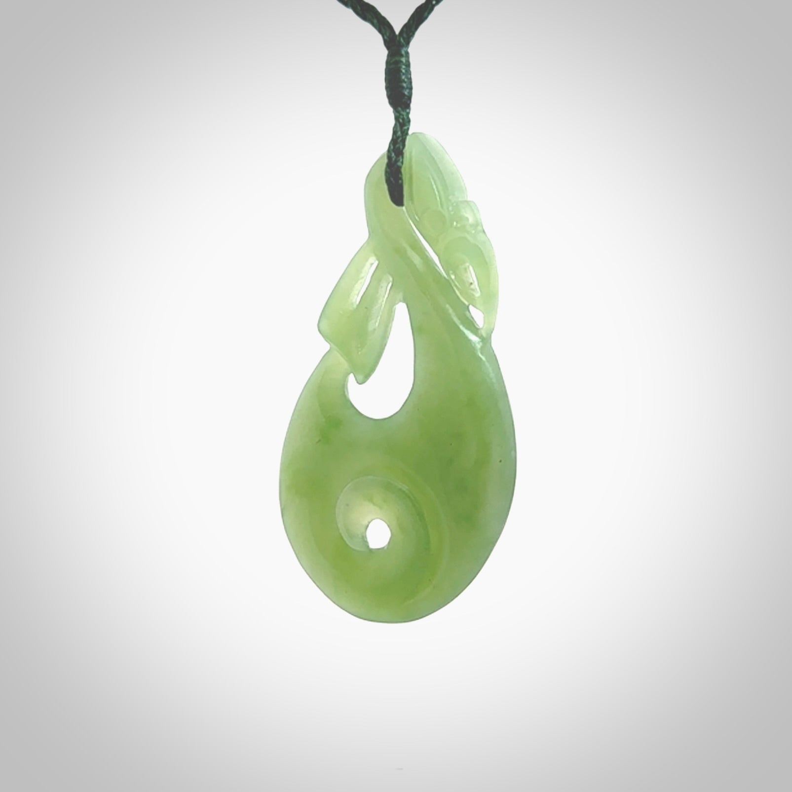 Hand carved New Zealand Inanga jade manaia with koru pendant. Carved from beautiful New Zealand Jade for NZ Pacific by Ross Crump. Unique jade jewellery for sale online. Provided with an adjustable manuka green cord.