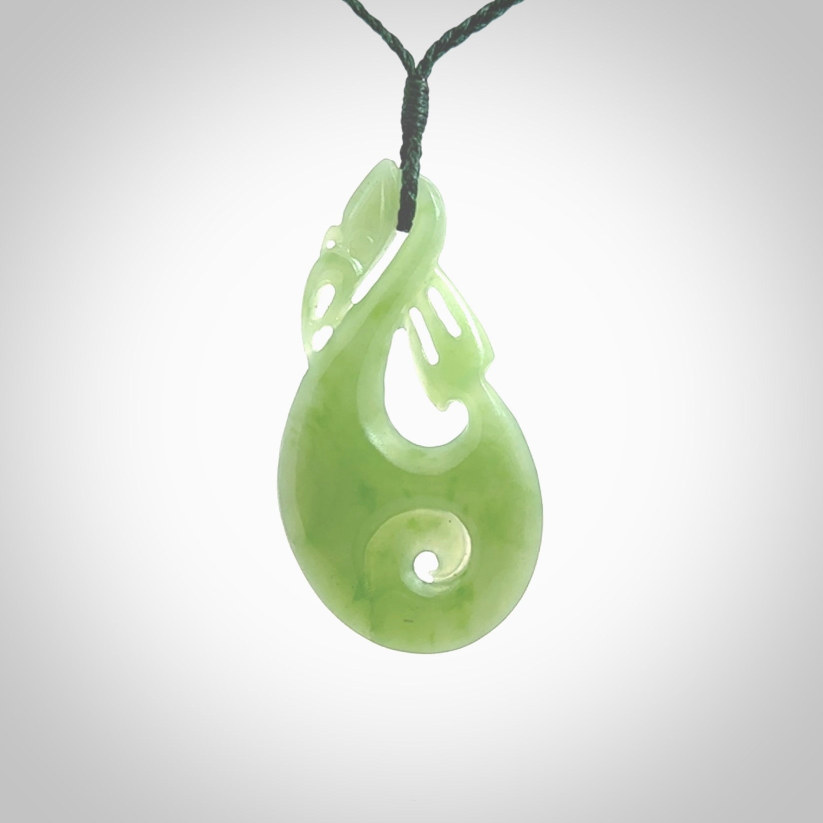 Hand carved New Zealand Inanga jade manaia with koru pendant. Carved from beautiful New Zealand Jade for NZ Pacific by Ross Crump. Unique jade jewellery for sale online. Provided with an adjustable manuka green cord.