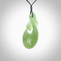 Hand carved New Zealand Inanga jade manaia with koru pendant. Carved from beautiful New Zealand Jade for NZ Pacific by Ross Crump. Unique jade jewellery for sale online. Provided with an adjustable manuka green cord.