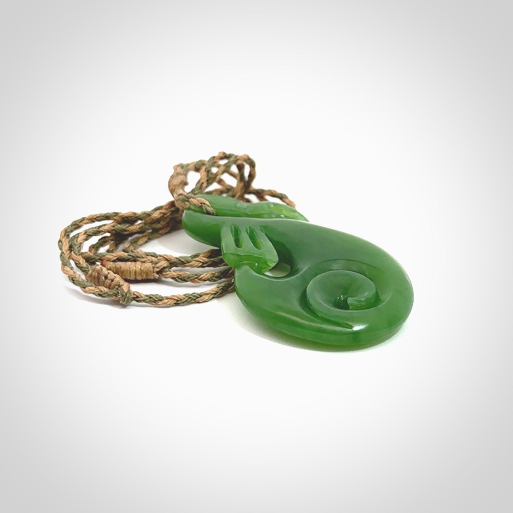 Hand carved New Zealand Kahurangi jade manaia with koru pendant. Carved from beautiful New Zealand Jade for NZ Pacific by Ross Crump. Unique jade jewellery for sale online. Provided with an adjustable tan/khaki cord.