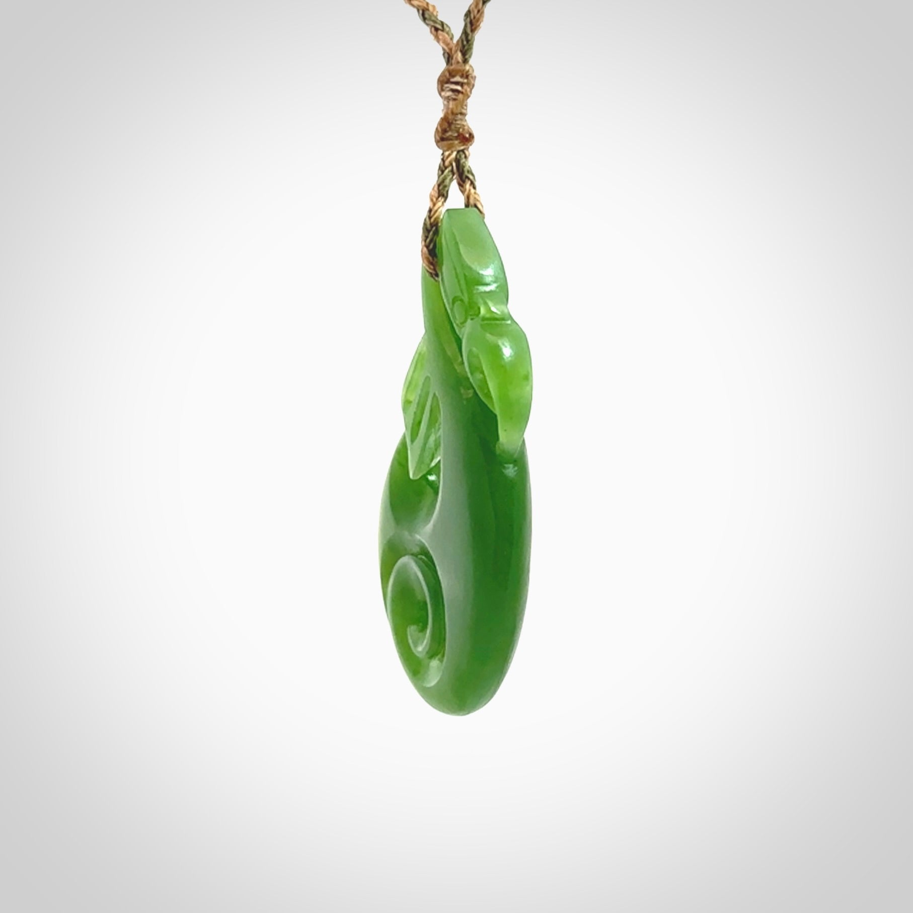 Hand carved New Zealand Kahurangi jade manaia with koru pendant. Carved from beautiful New Zealand Jade for NZ Pacific by Ross Crump. Unique jade jewellery for sale online. Provided with an adjustable tan/khaki cord.