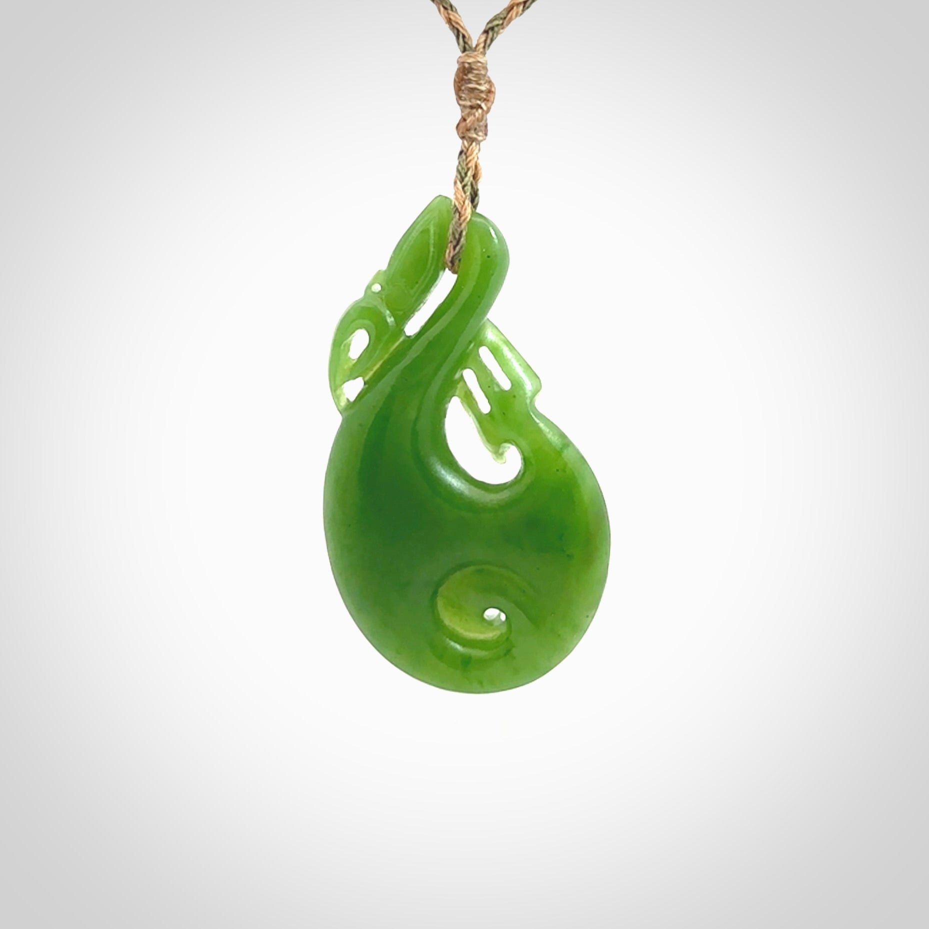 Hand carved New Zealand Kahurangi jade manaia with koru pendant. Carved from beautiful New Zealand Jade for NZ Pacific by Ross Crump. Unique jade jewellery for sale online. Provided with an adjustable tan/khaki cord.