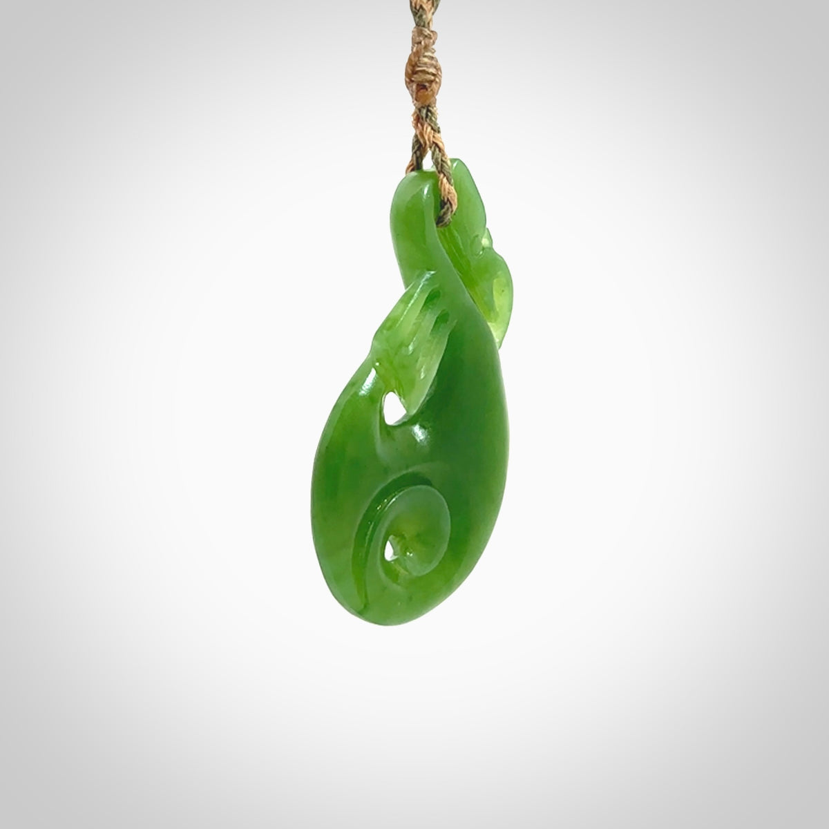 Hand carved New Zealand Kahurangi jade manaia with koru pendant. Carved from beautiful New Zealand Jade for NZ Pacific by Ross Crump. Unique jade jewellery for sale online. Provided with an adjustable tan/khaki cord.