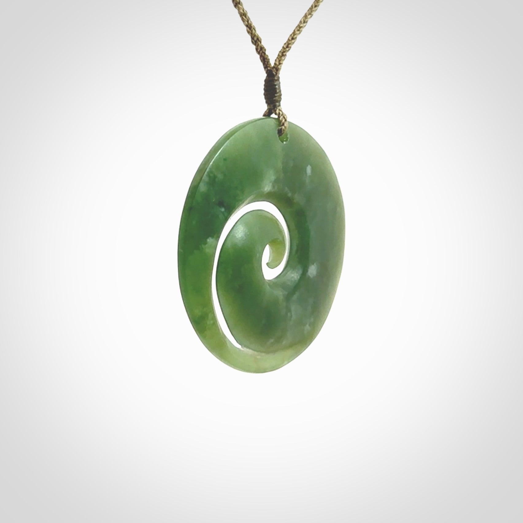 This picture shows a hand carved jade koru pendant. It is a beautiful green colour and is a wonderful, large sized piece of jewellery. The cord is a four plait olive colour and adjustable so that you can position the pendant where it suits you best. This koru was carved for us by Ric Moor. Delivery is free worldwide.