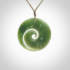 This picture shows a hand carved jade koru pendant. It is a beautiful green colour and is a wonderful, large sized piece of jewellery. The cord is a four plait olive colour and adjustable so that you can position the pendant where it suits you best. This koru was carved for us by Ric Moor. Delivery is free worldwide.