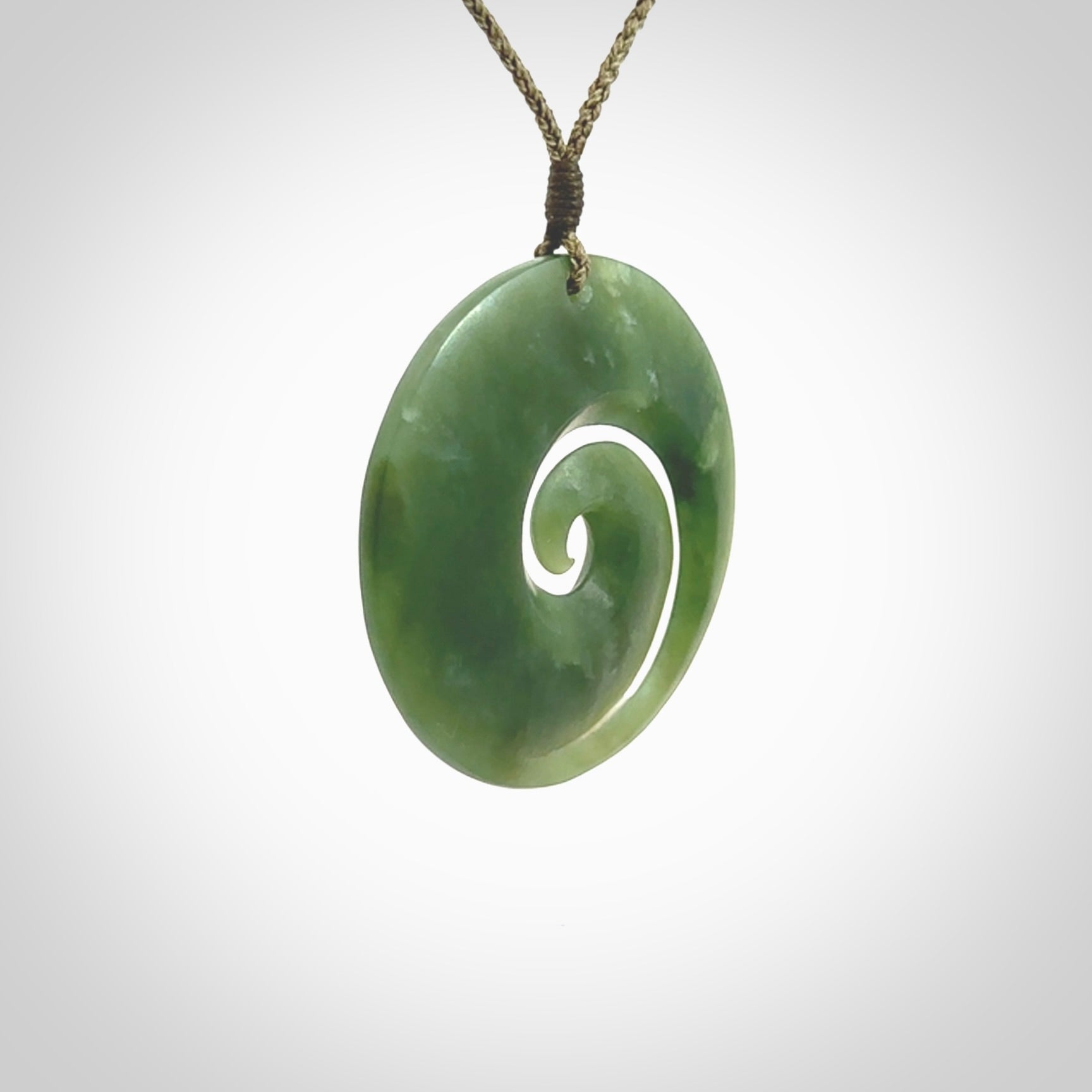 This picture shows a hand carved jade koru pendant. It is a beautiful green colour and is a wonderful, large sized piece of jewellery. The cord is a four plait olive colour and adjustable so that you can position the pendant where it suits you best. This koru was carved for us by Ric Moor. Delivery is free worldwide.