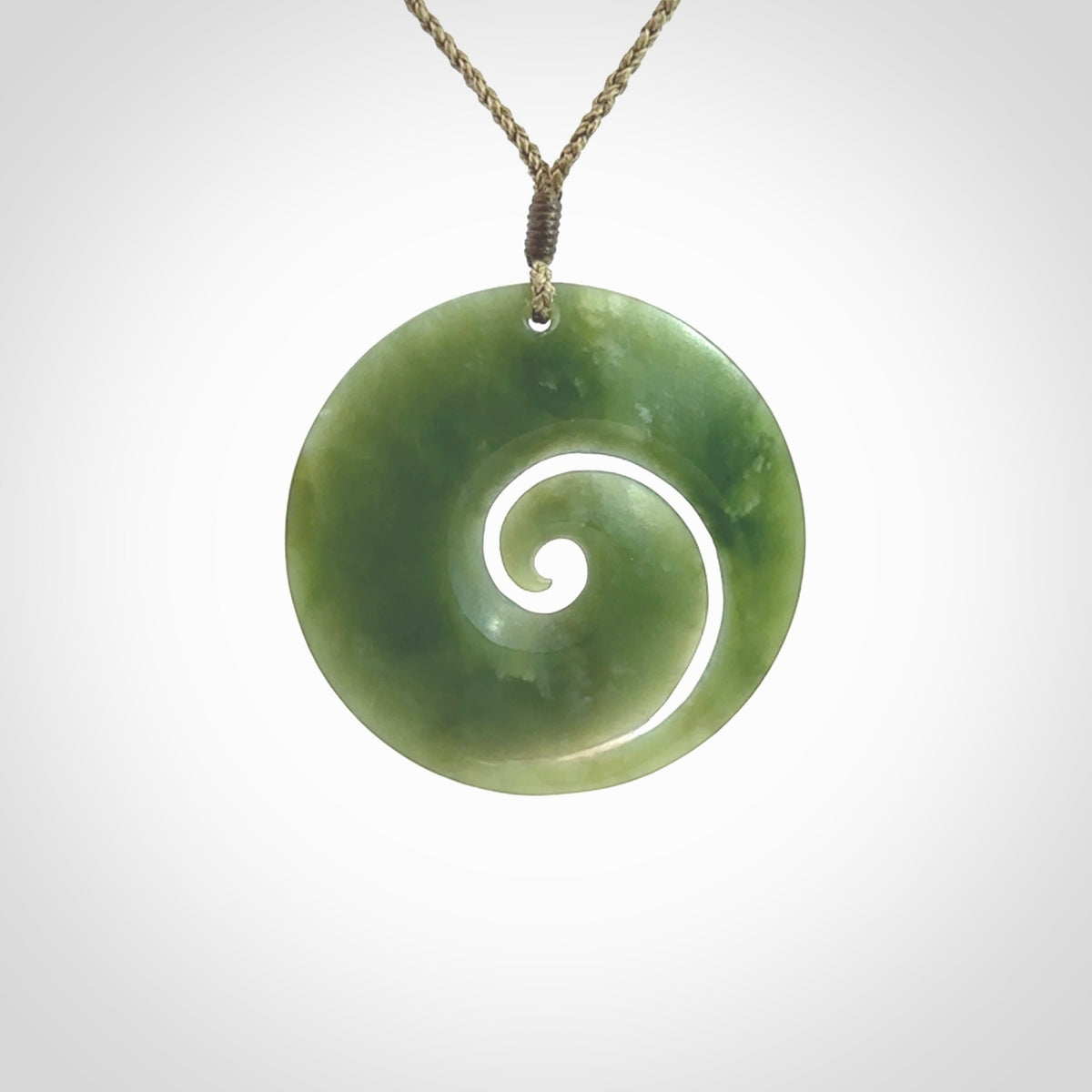 This picture shows a hand carved jade koru pendant. It is a beautiful green colour and is a wonderful, large sized piece of jewellery. The cord is a four plait olive colour and adjustable so that you can position the pendant where it suits you best. This koru was carved for us by Ric Moor. Delivery is free worldwide.