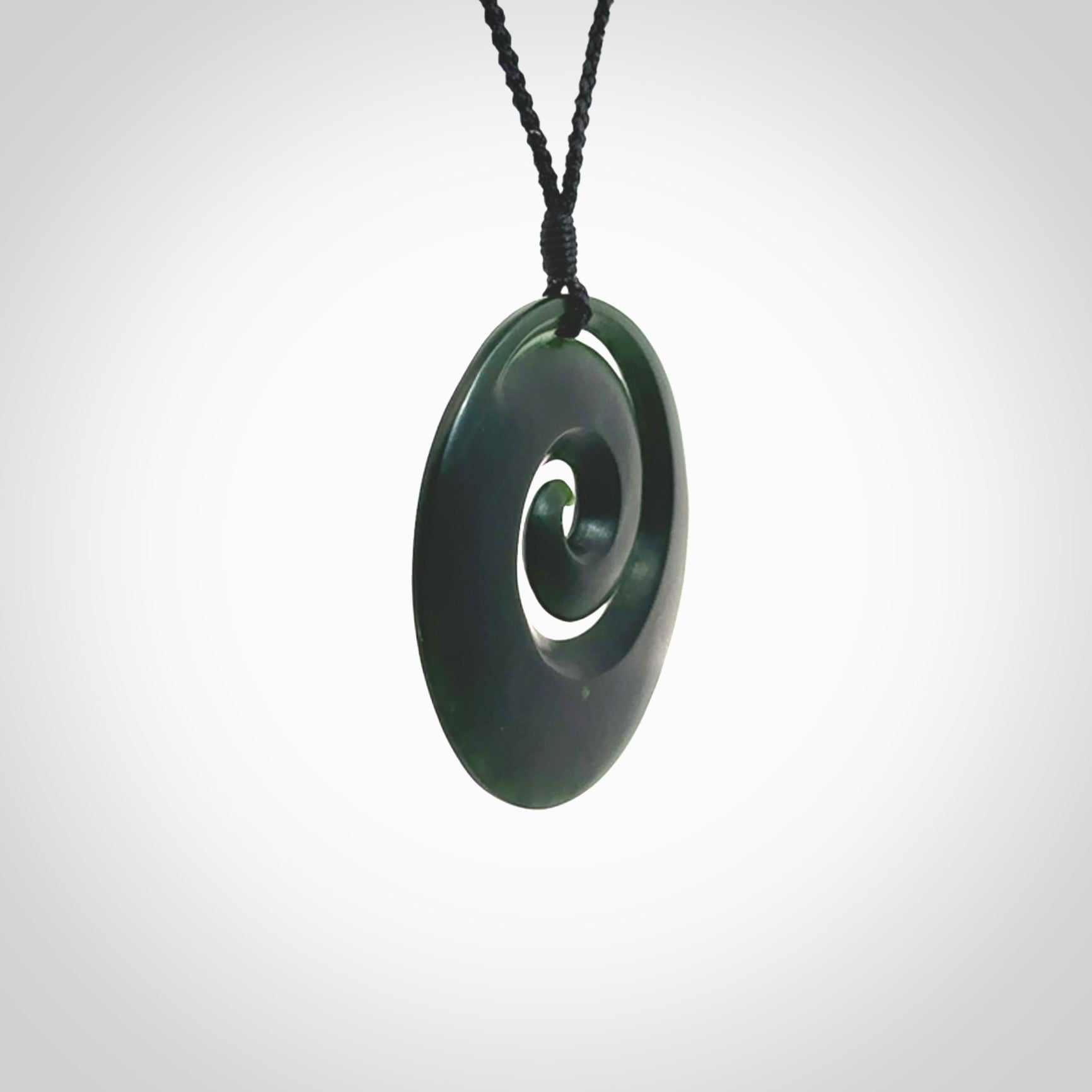 This is a large deep and dark green New Zealand jade koru pendant. We have bound this with a black coloured cord necklace. The necklace is adjustable so you can position the piece where it suits you the best. Hand made by Ric Moor.