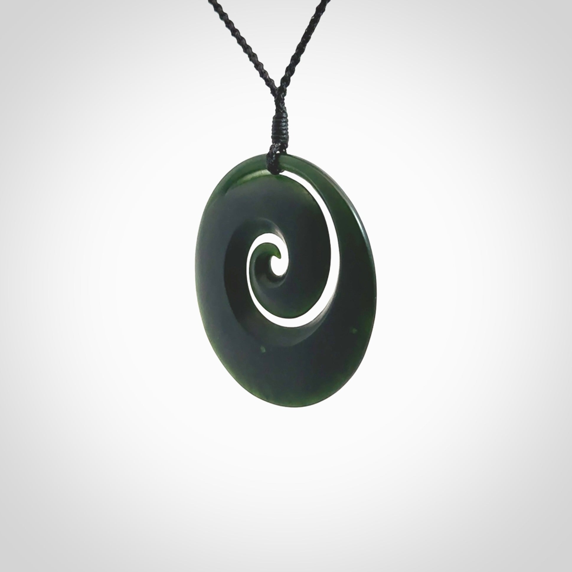 This is a large deep and dark green New Zealand jade koru pendant. We have bound this with a black coloured cord necklace. The necklace is adjustable so you can position the piece where it suits you the best. Hand made by Ric Moor.