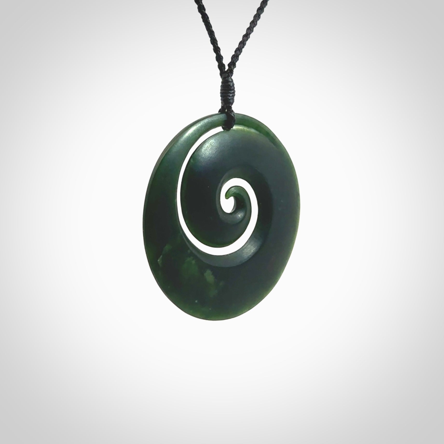 This is a large deep and dark green New Zealand jade koru pendant. We have bound this with a black coloured cord necklace. The necklace is adjustable so you can position the piece where it suits you the best. Hand made by Ric Moor.