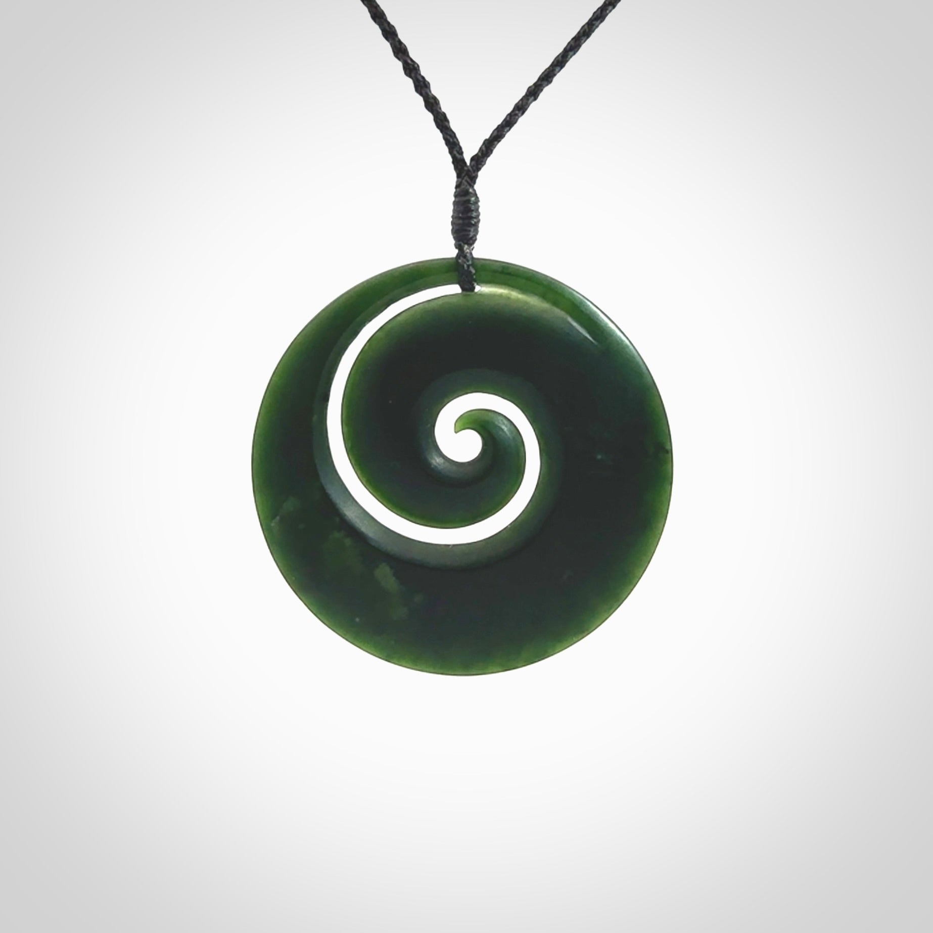 This is a large deep and dark green New Zealand jade koru pendant. We have bound this with a black coloured cord necklace. The necklace is adjustable so you can position the piece where it suits you the best. Hand made by Ric Moor.