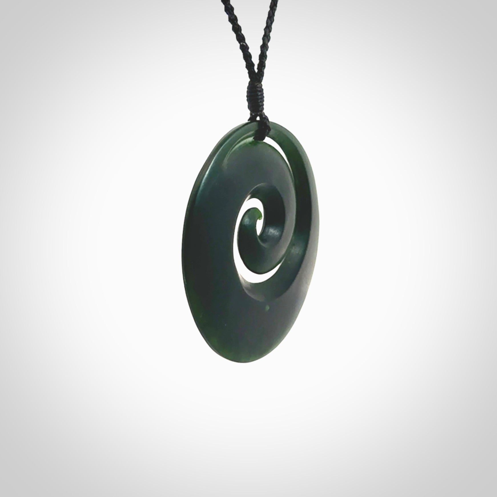 This is a large deep and dark green New Zealand jade koru pendant. We have bound this with a black coloured cord necklace. The necklace is adjustable so you can position the piece where it suits you the best. Hand made by Ric Moor.