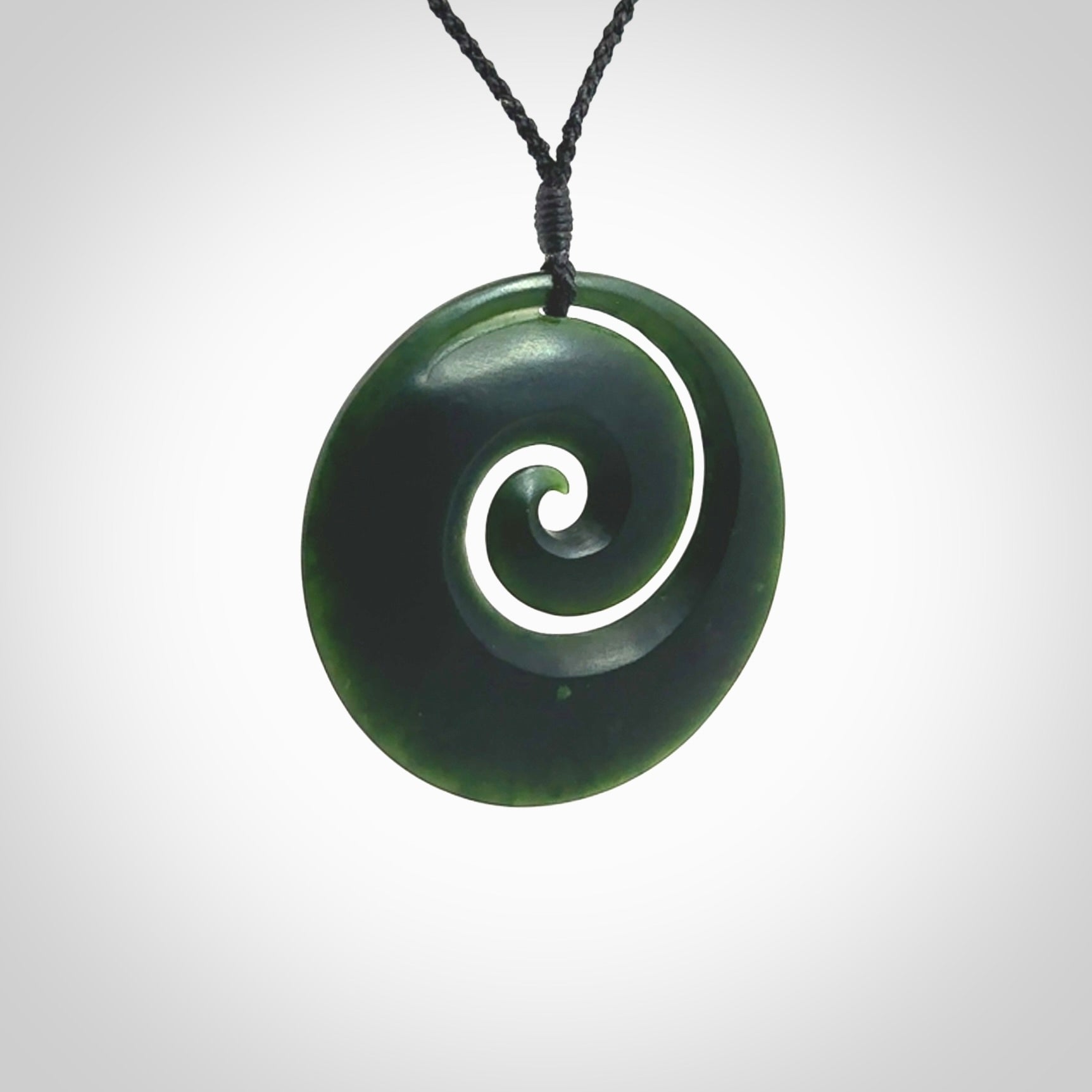 This is a large deep and dark green New Zealand jade koru pendant. We have bound this with a black coloured cord necklace. The necklace is adjustable so you can position the piece where it suits you the best. Hand made by Ric Moor.